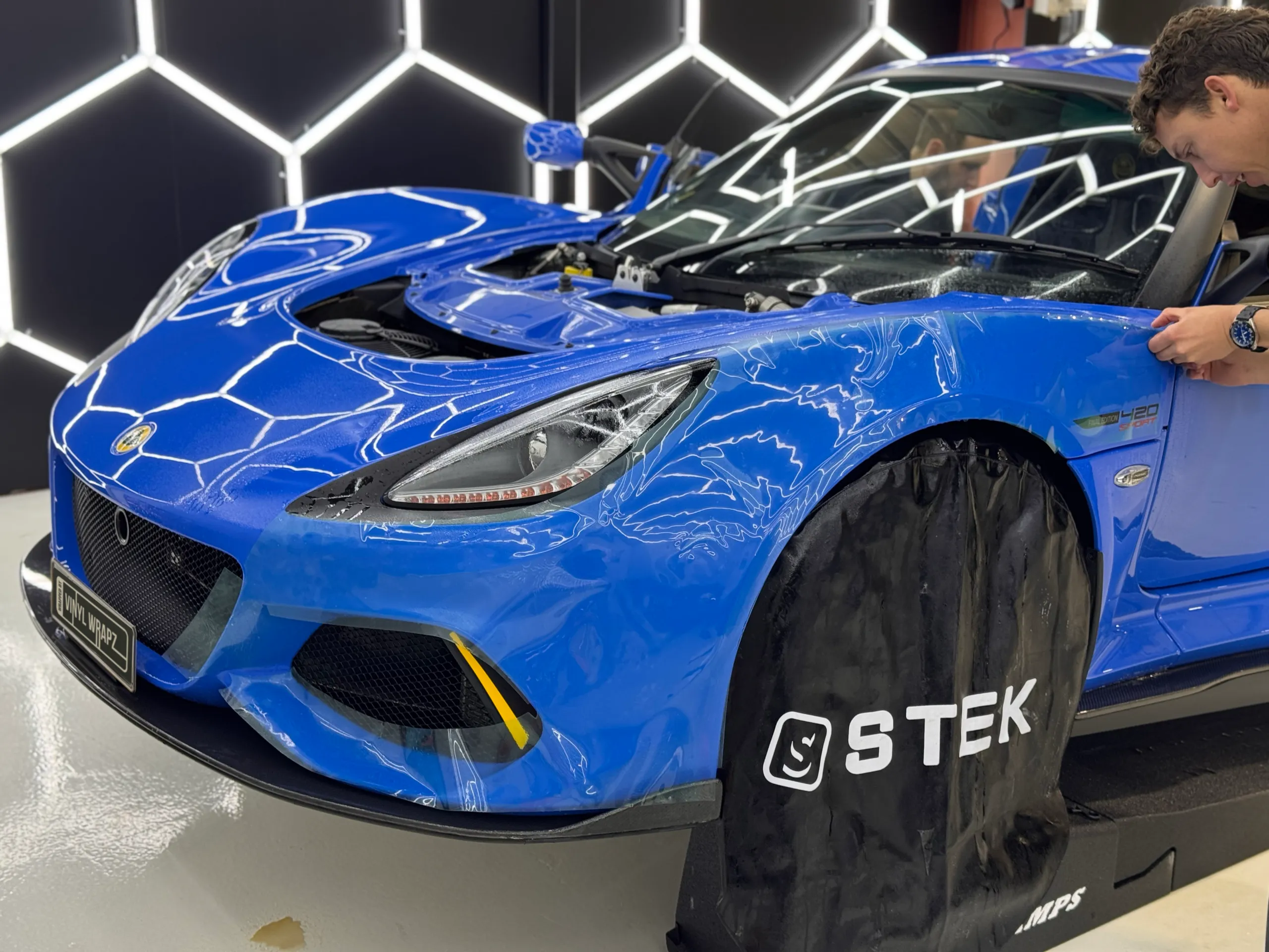 Close view of an installer fitting film around the blue Lotus Exige front wheel arch