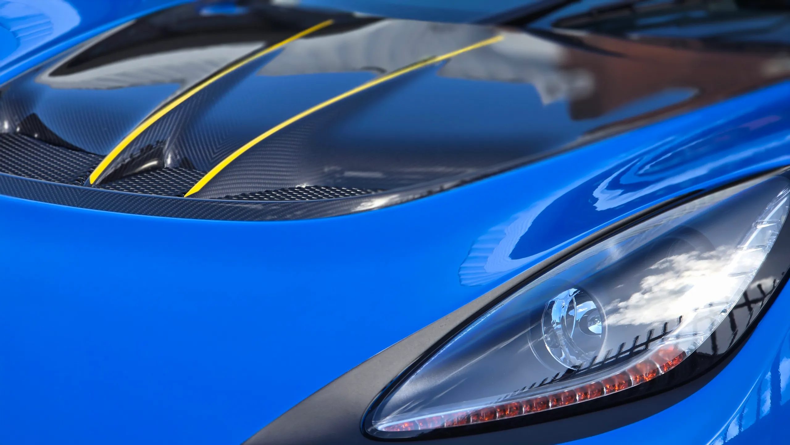 Carbon bonnet panel with yellow stripes beside the blue Lotus Exige headlight