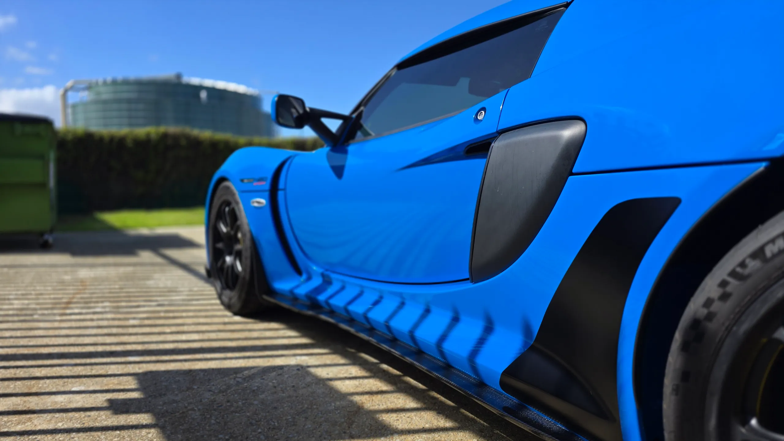 Low side detail of the blue Lotus Exige door, black air intake and rear wheel