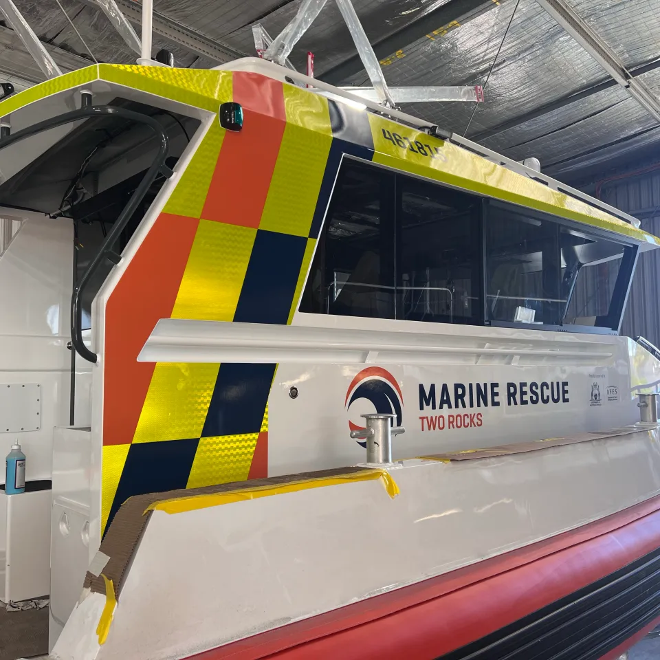 Marine Rescue Two Rocks cabin with orange, yellow and navy graphics during installation, with masking tape along edges