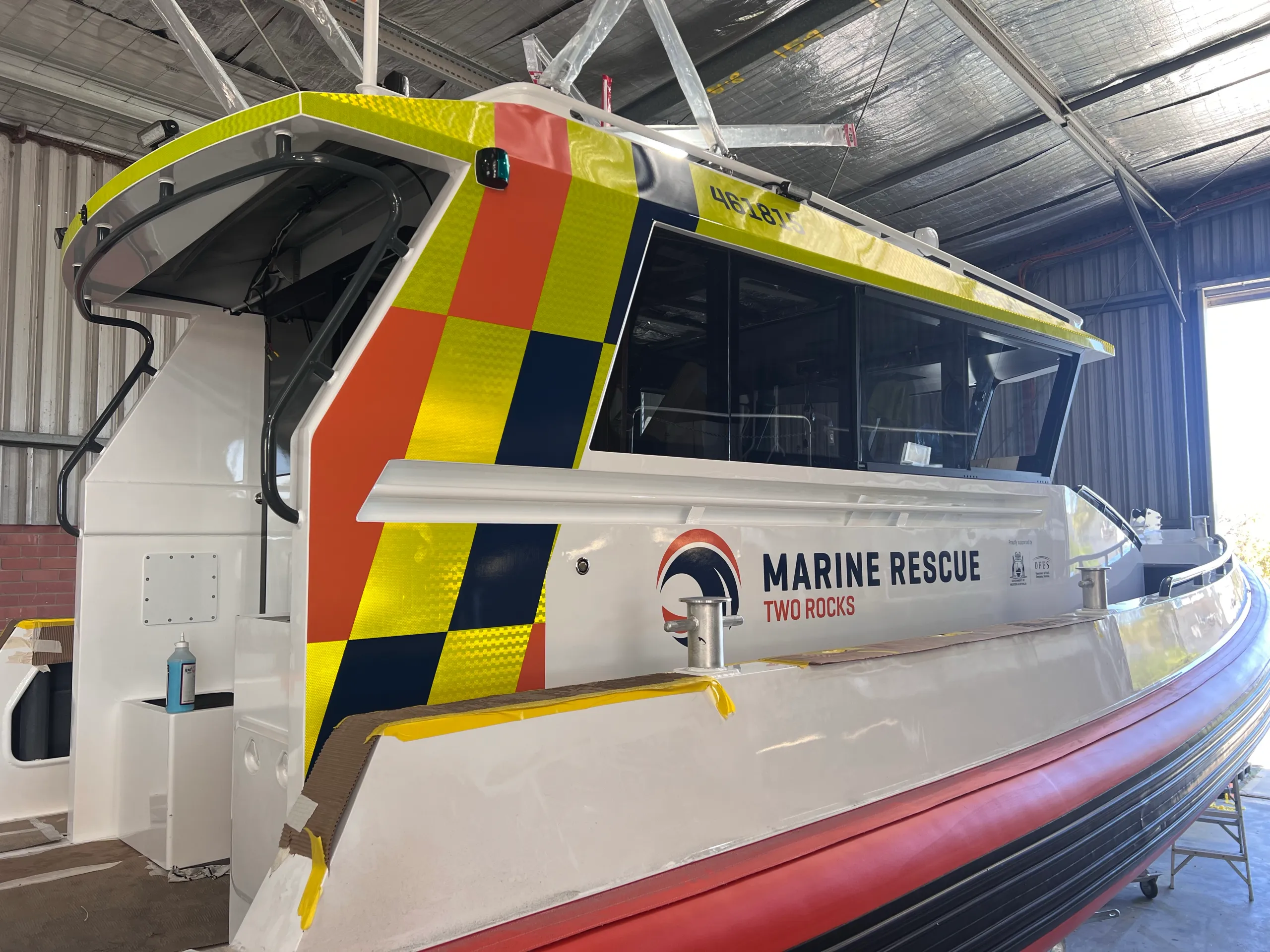 Marine Rescue Two Rocks cabin with orange, yellow and navy graphics during installation, with masking tape along edges