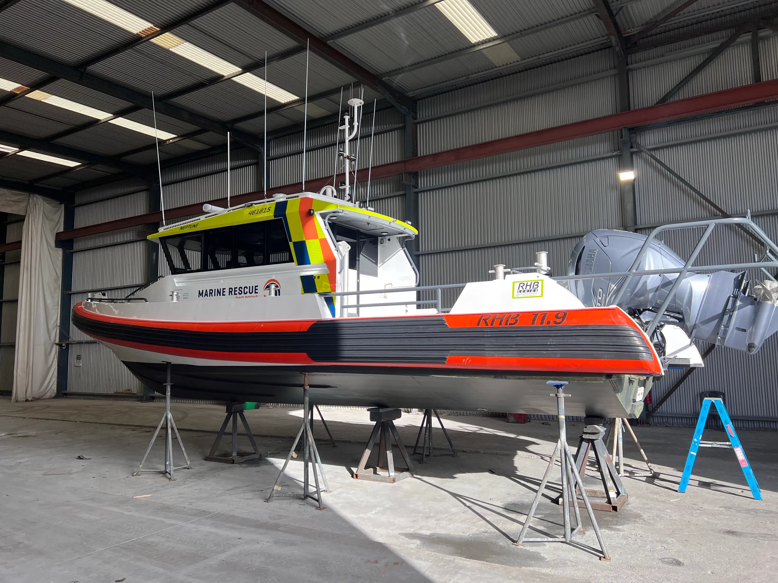 Marine Rescue boat Neptune on stands inside a shed, showing its orange hull trim and high-visibility cabin graphics