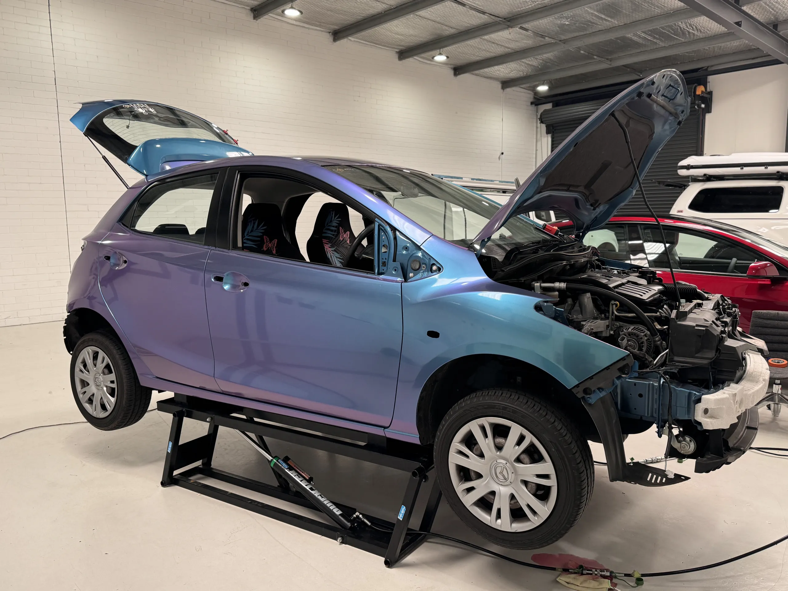 Turquoise and lavender Mazda 2 during wrapping in the workshop, front quarter