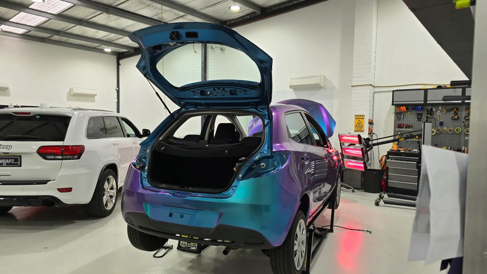 Turquoise and lavender Mazda 2 during wrapping in the workshop, rear quarter