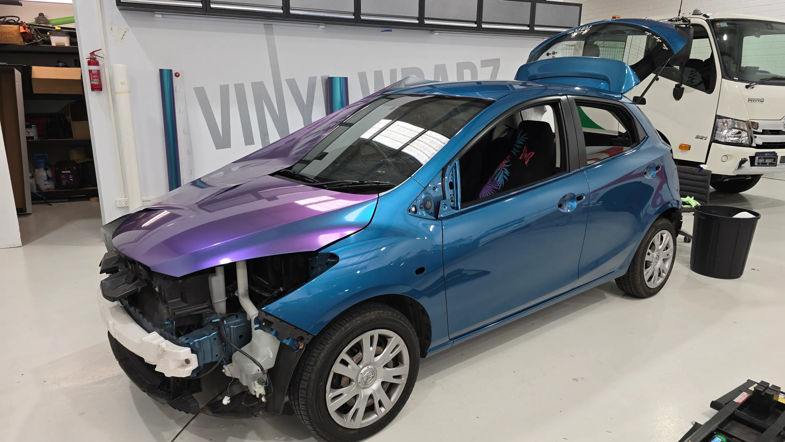 Turquoise and lavender Mazda 2 during wrapping in the workshop, front quarter