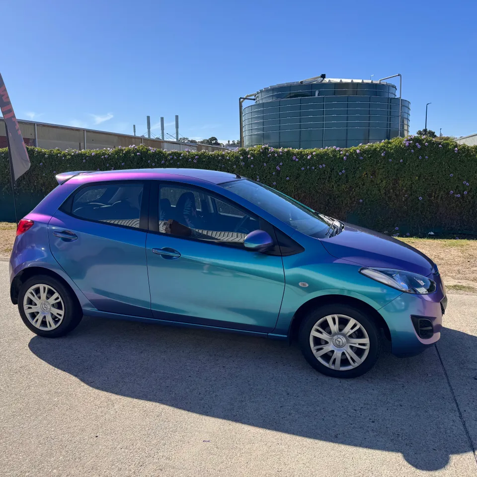 Turquoise and lavender Mazda 2 during wrapping in the workshop, side