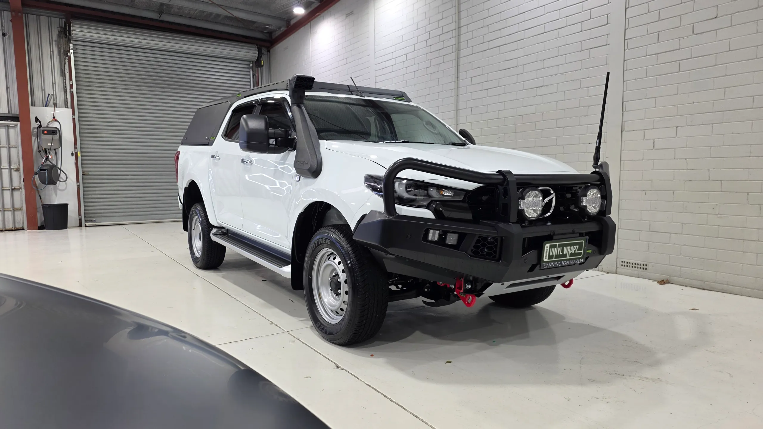 White Mazda BT-50 with a bullbar, snorkel and black canopy in the workshop