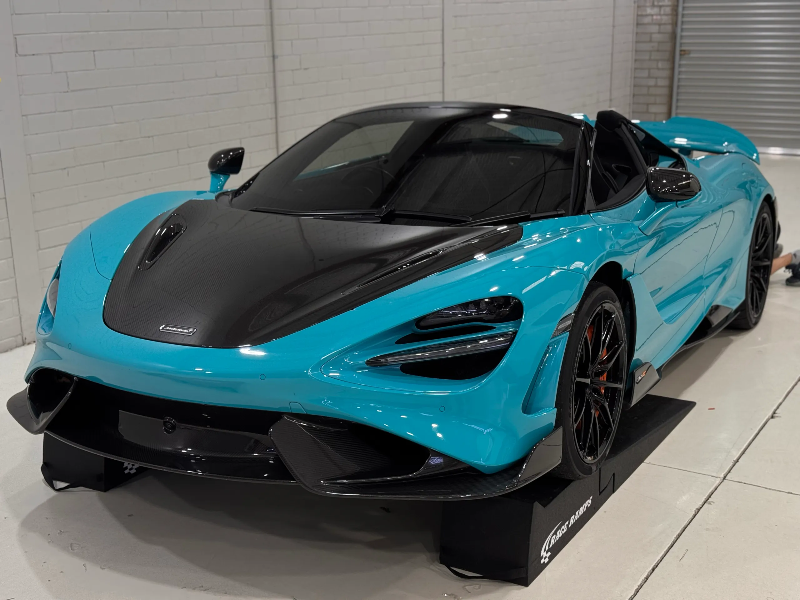 Blue open-top McLaren with a carbon bonnet, black wheels and front splitter in the workshop