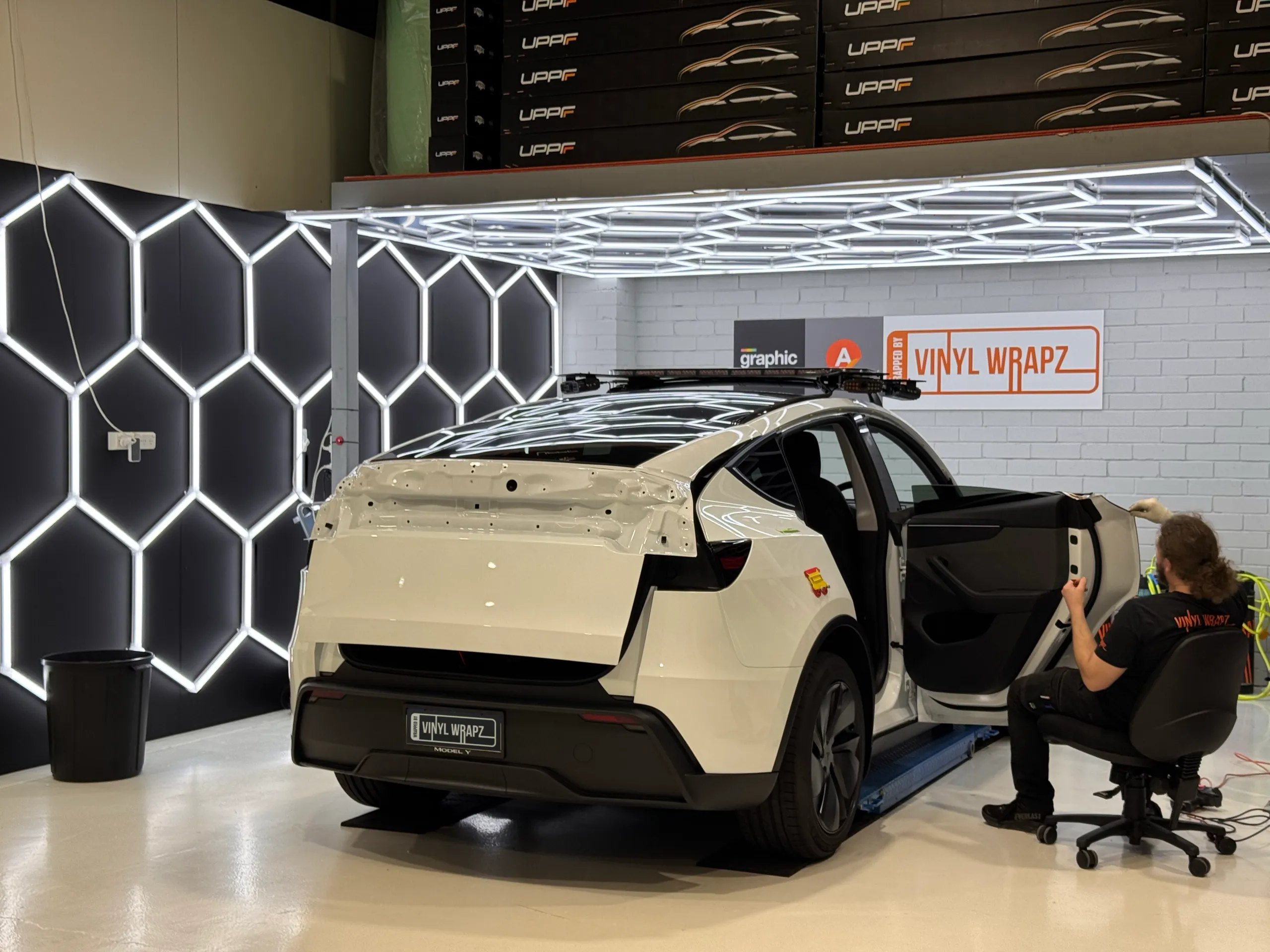 Back-facing installer working beside a white Tesla Model Y with rear trim removed