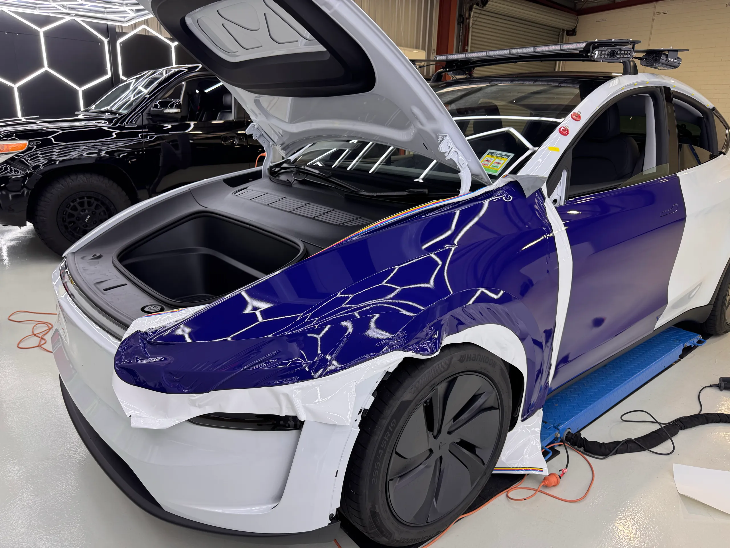 Blue film being fitted to a white Tesla Model Y with its bonnet raised