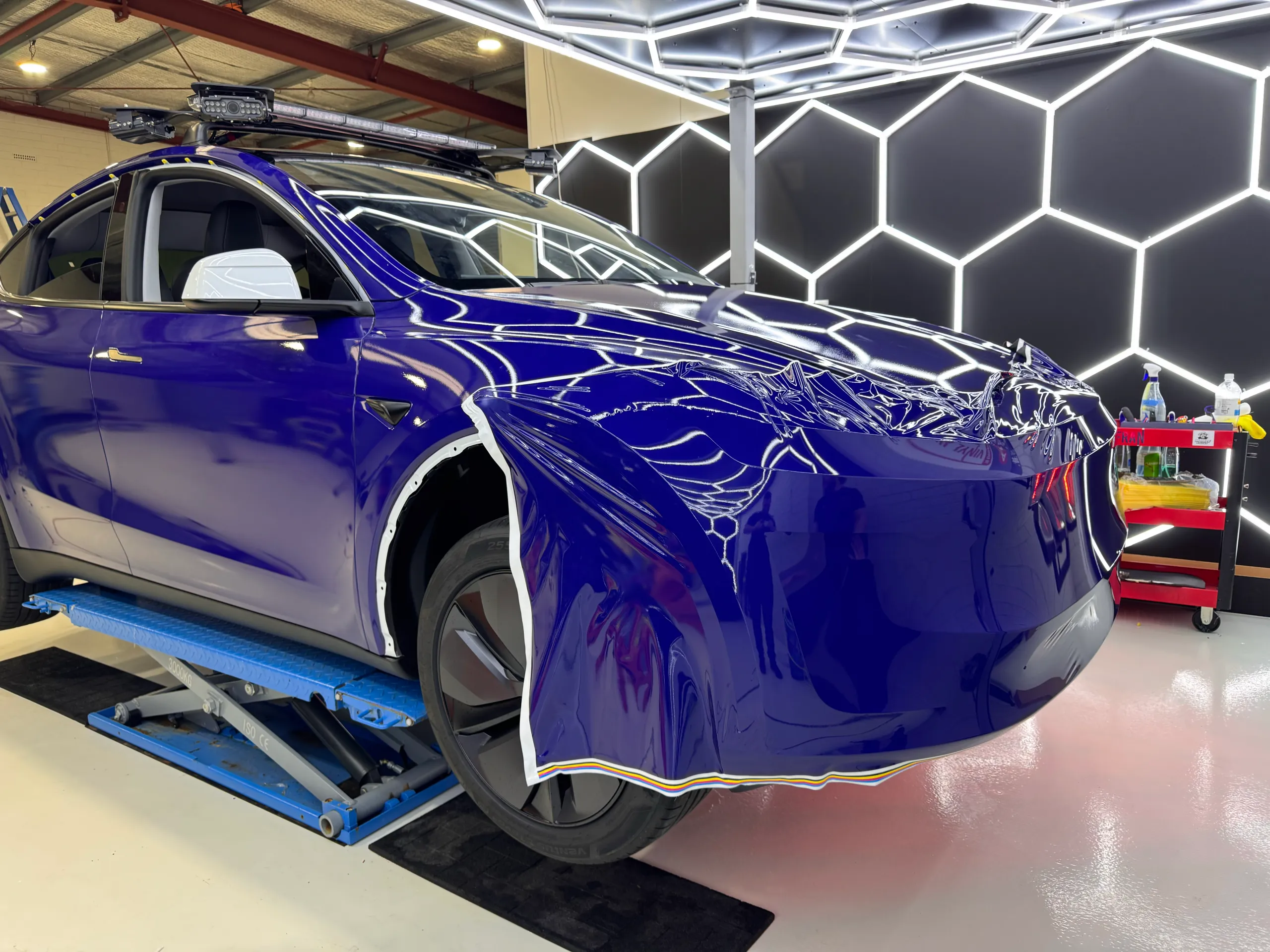 Blue film draped across the Tesla Model Y front bumper during wrapping