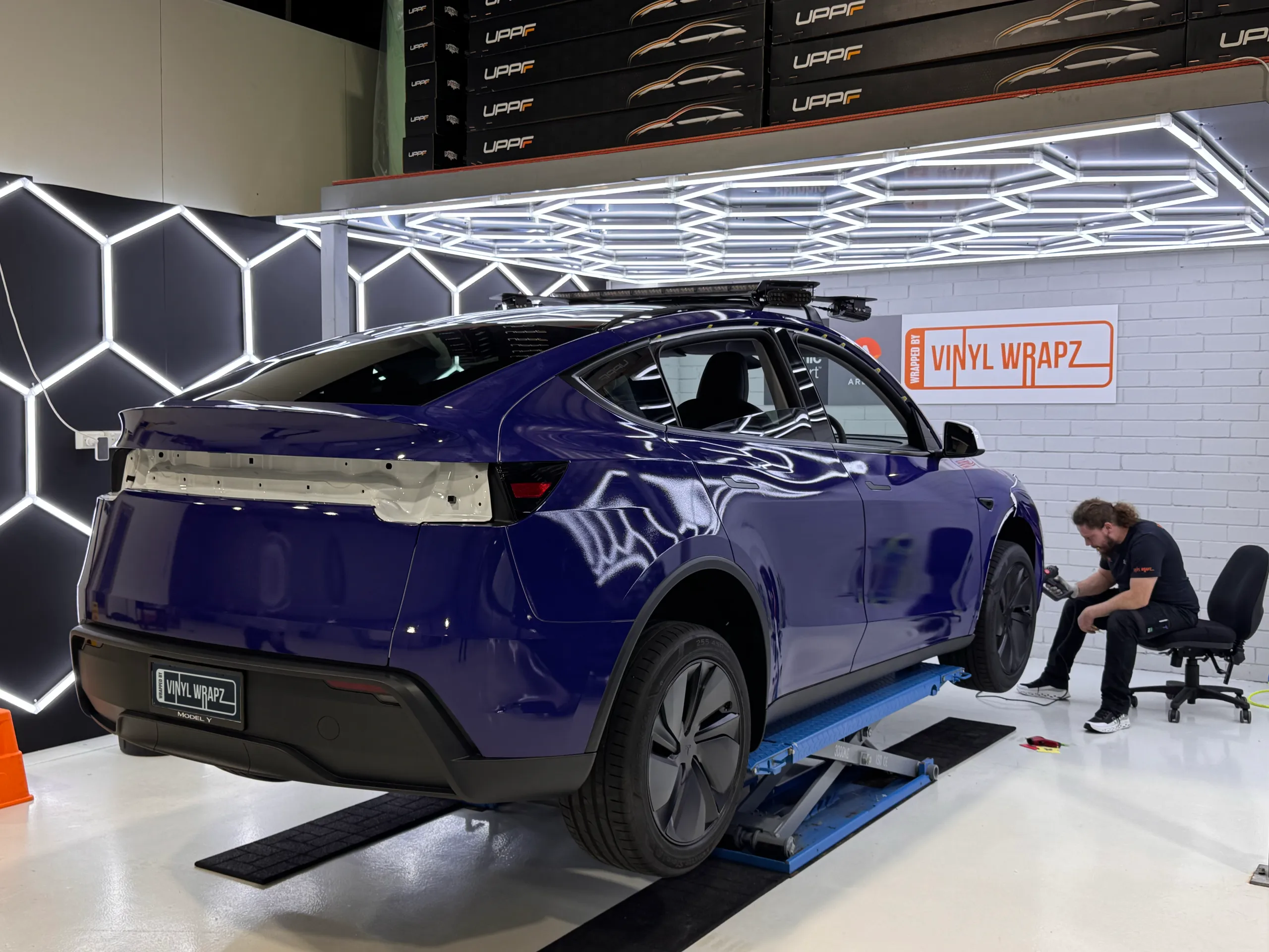 Installer working beside the blue Tesla Model Y with rear trim removed