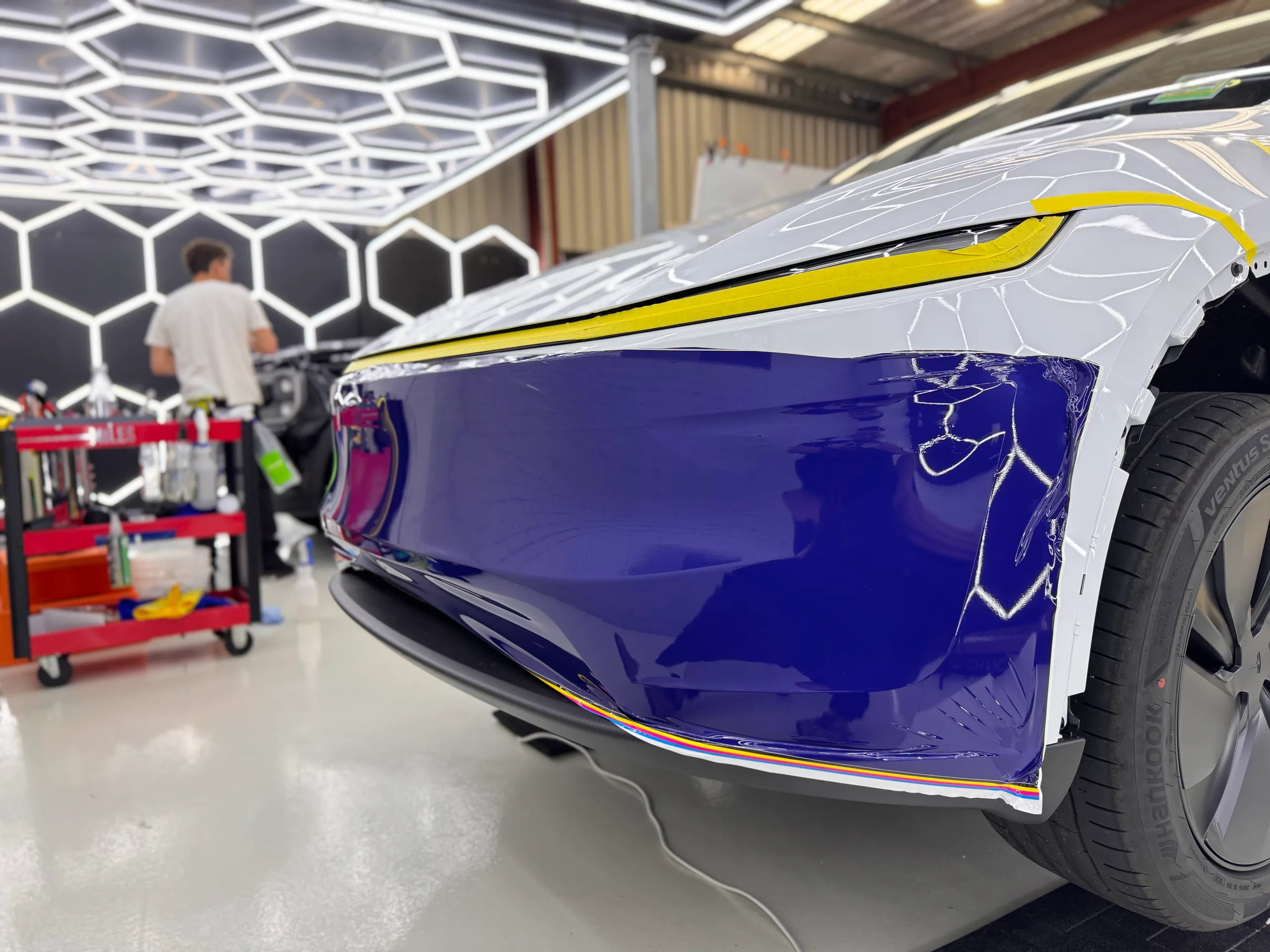 Blue film being fitted to the Tesla front bumper with its upper bodywork still white