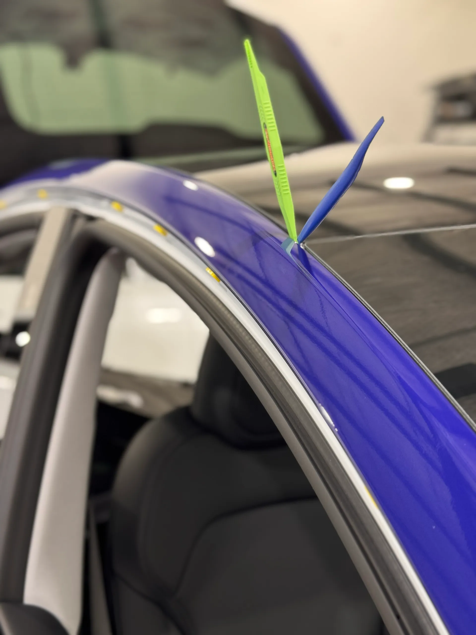 Tools positioned beside blue wrap film along the Tesla roof edge during installation