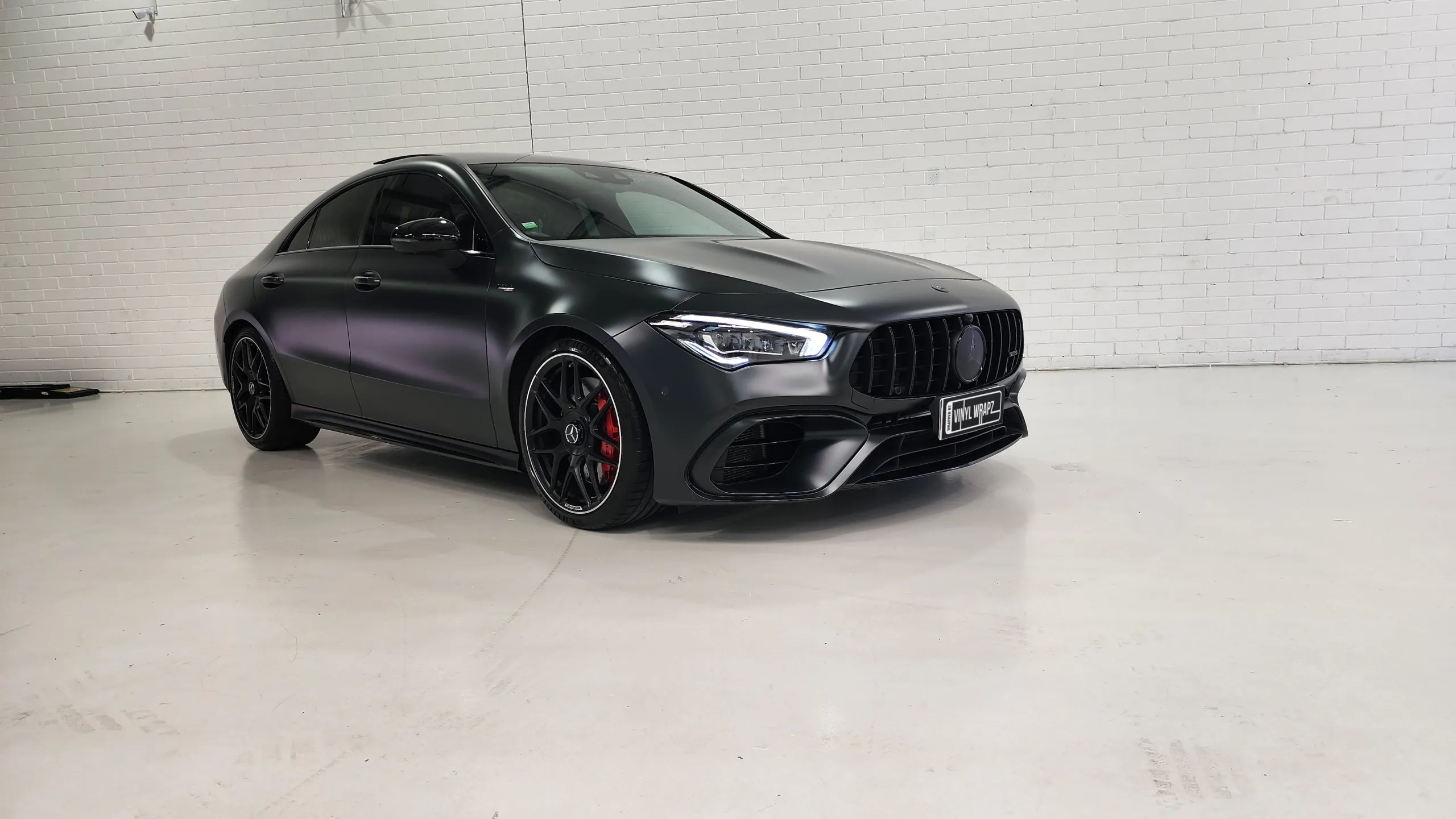Satin dark grey Mercedes-AMG CLA 45 S against a white workshop wall