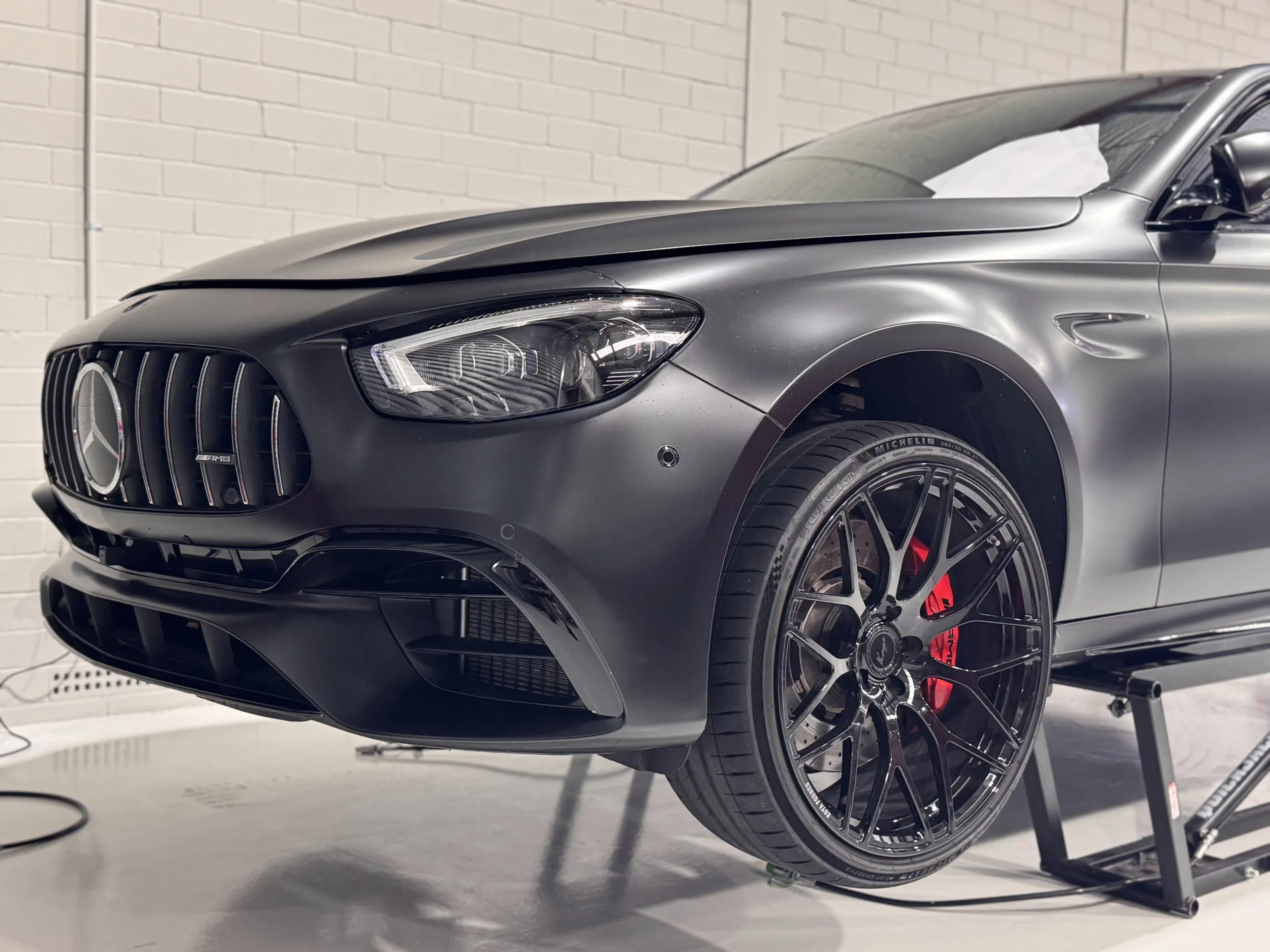 Satin black Mercedes-AMG E63 front corner on a workshop lift with its bonnet ajar