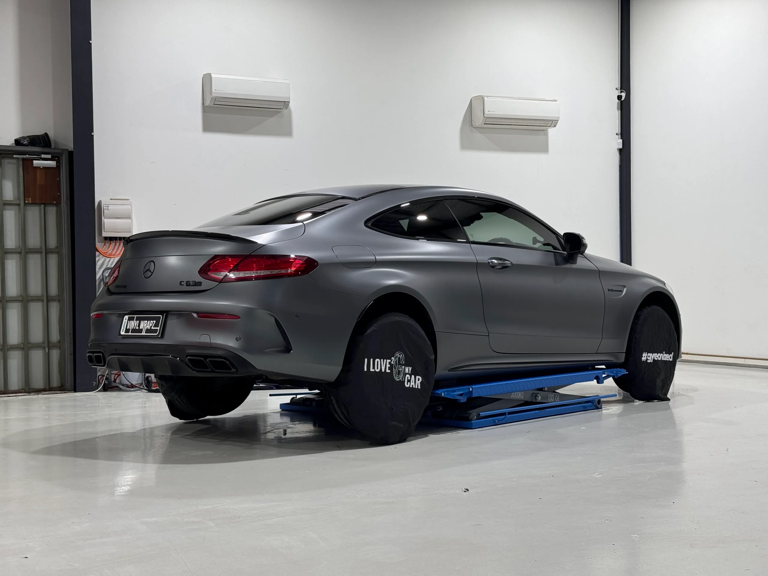 Rear-quarter view of a satin grey Mercedes-AMG C63 S coupe on a workshop lift