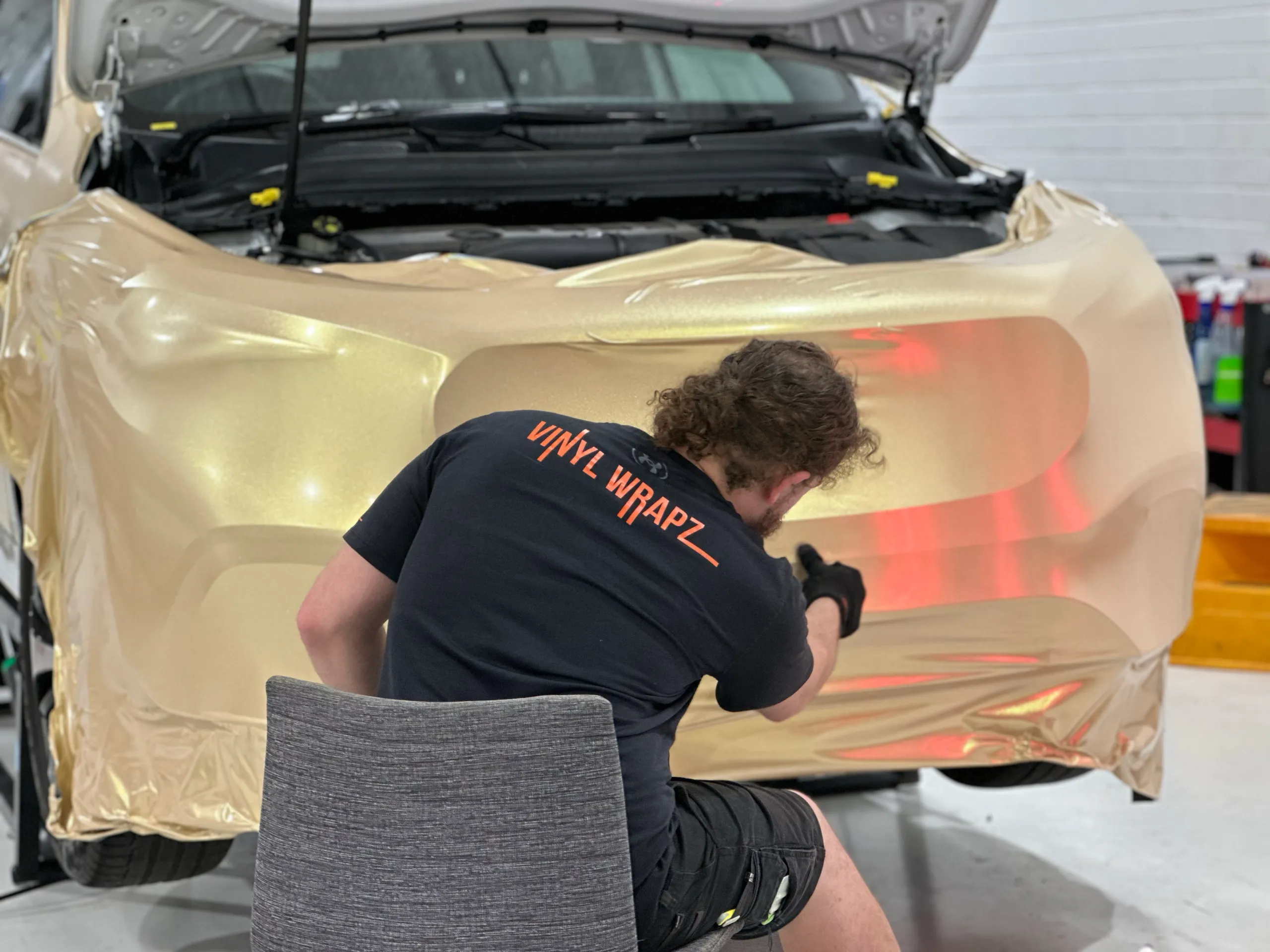 Installer shaping gold film across the Mercedes-Benz GLA front bumper