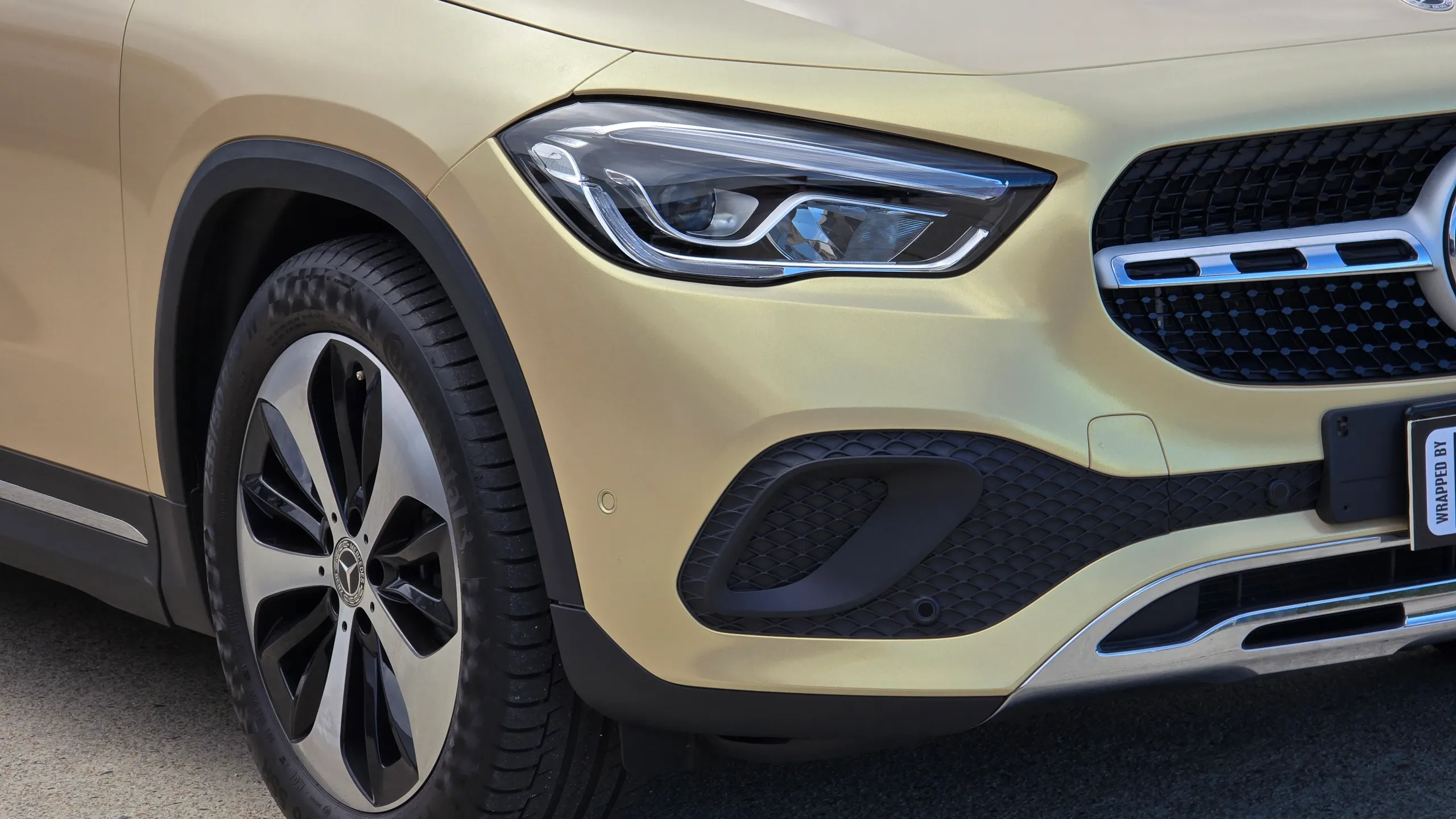 Gold Mercedes-Benz GLA front wheel, headlight and bumper outdoors