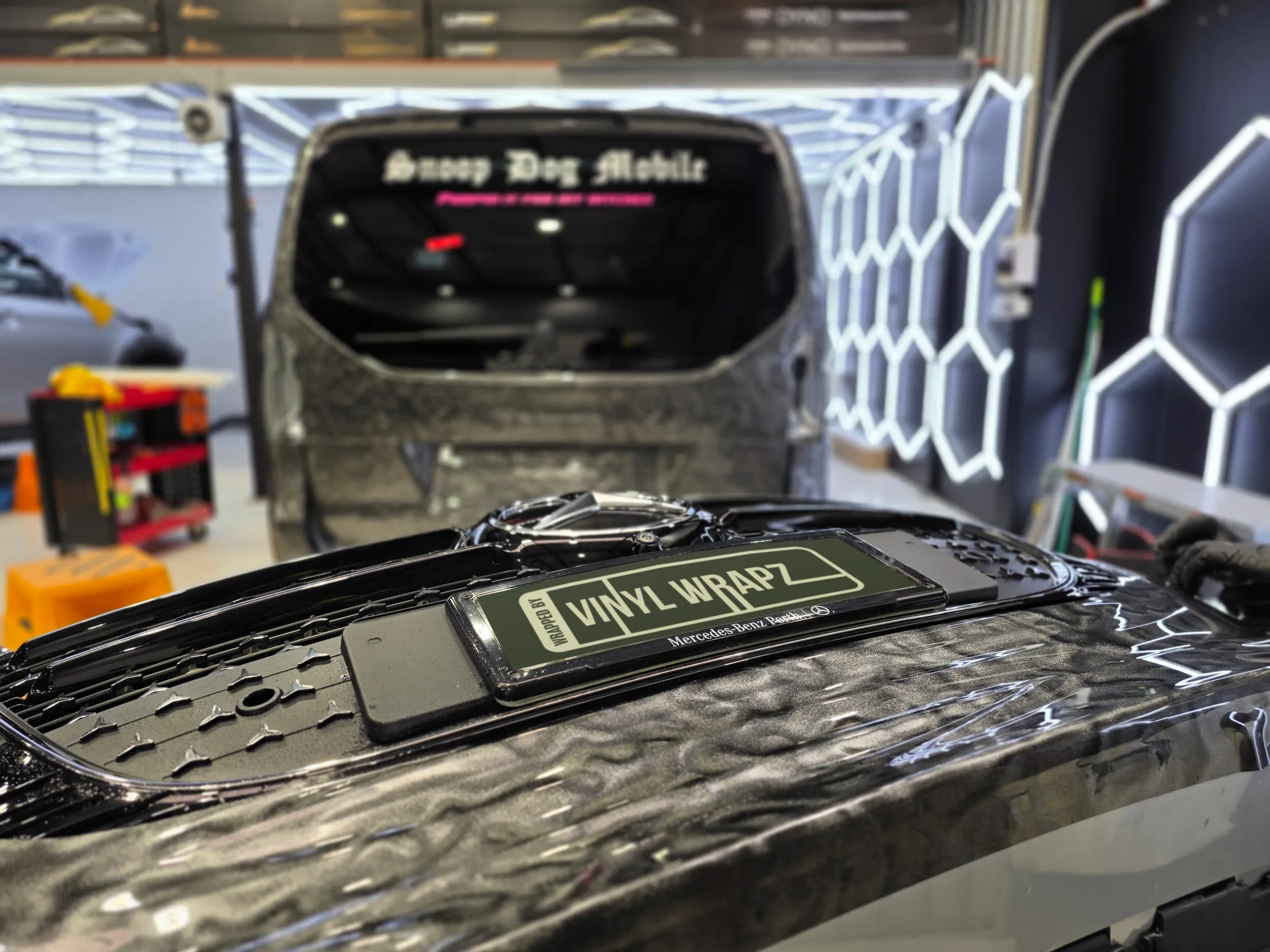 Removed Mercedes-Benz V-Class front bumper with patterned grey film, resting in front of the van