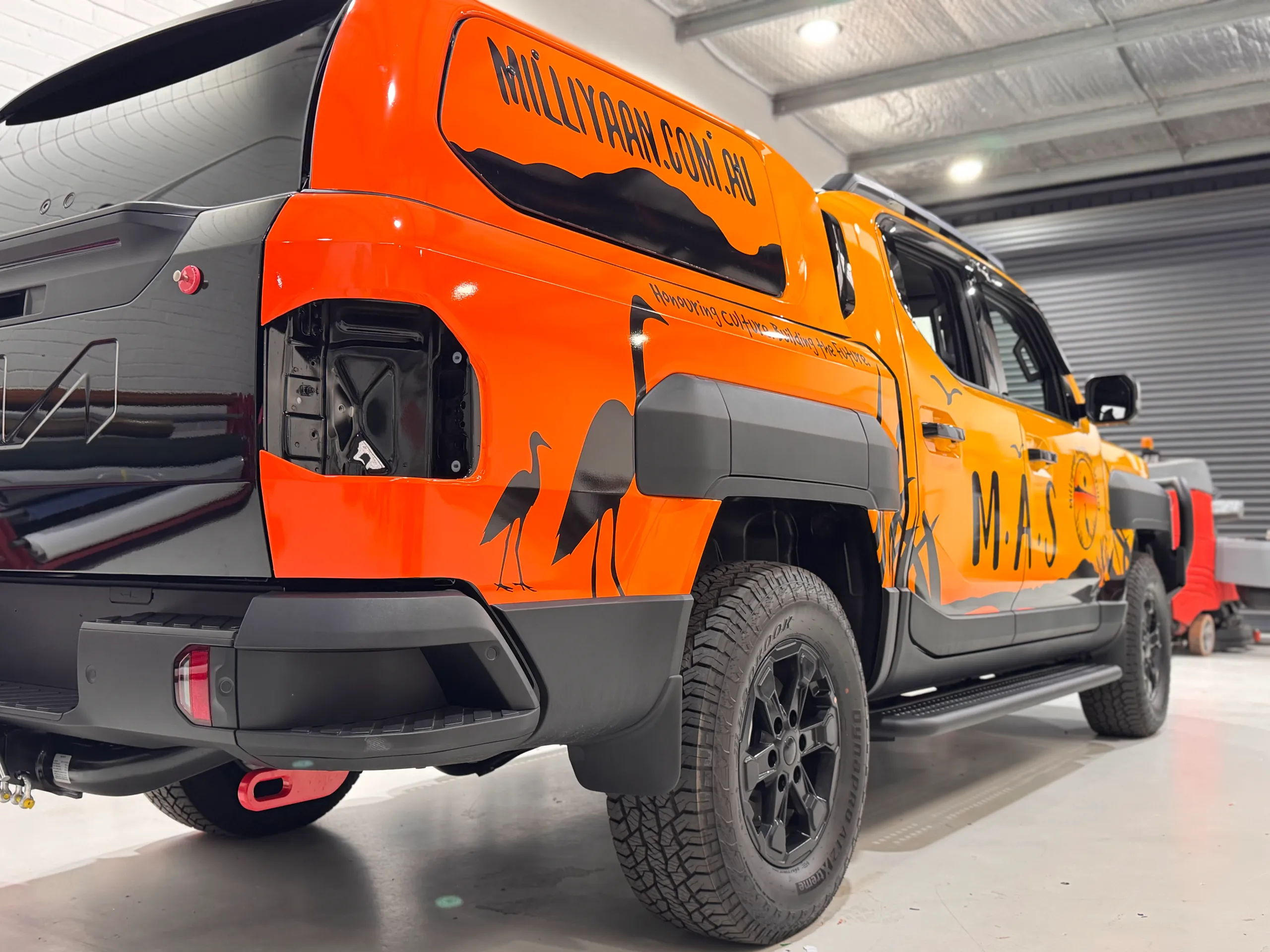 Kia Tasman with orange Milliyaan graphics in the workshop before rear-light refitting