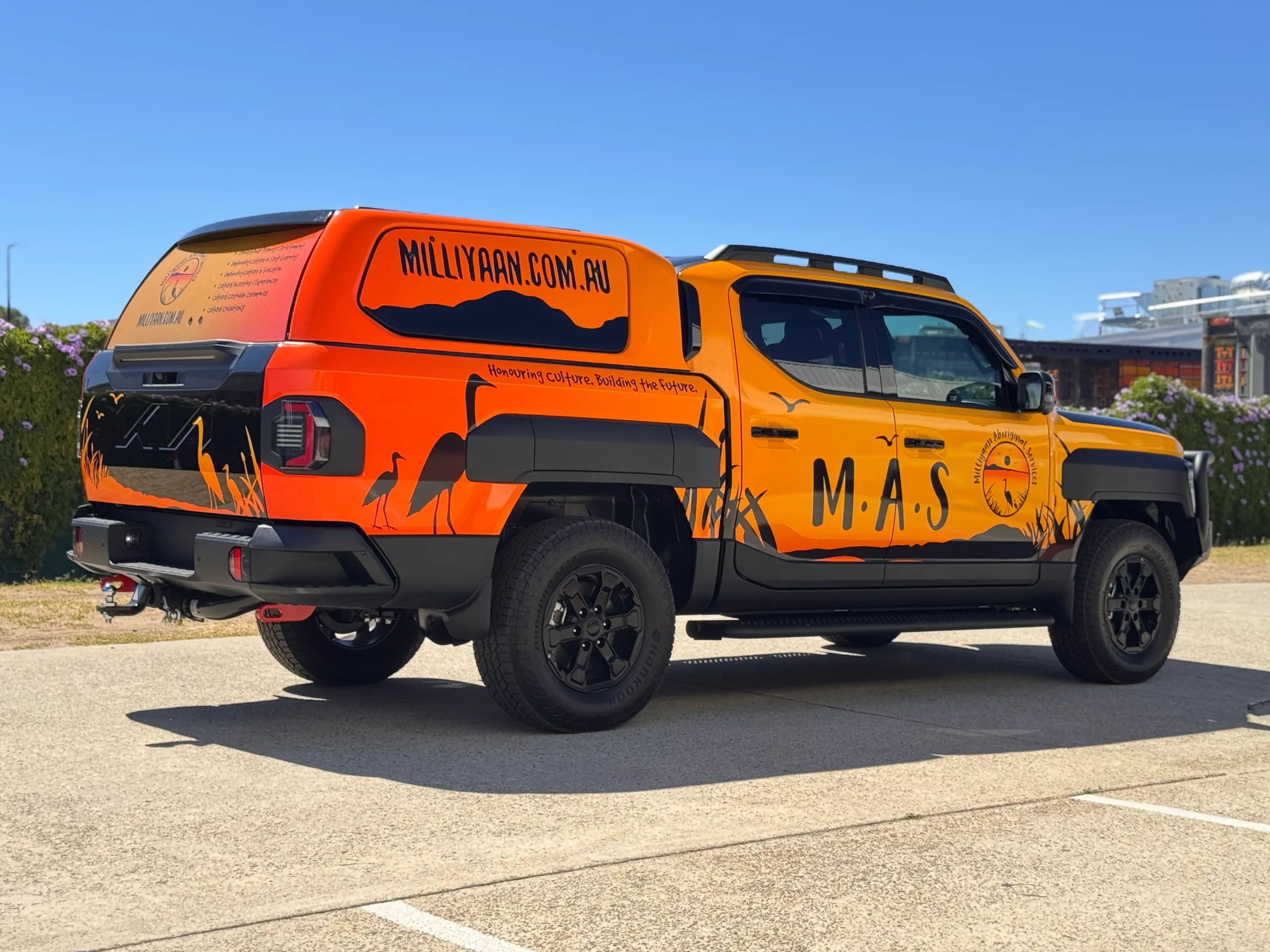 Orange and yellow Milliyaan Aboriginal Services graphics across the Kia Tasman and canopy
