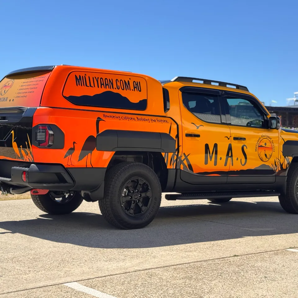 Orange and yellow Milliyaan Aboriginal Services graphics across the Kia Tasman and canopy