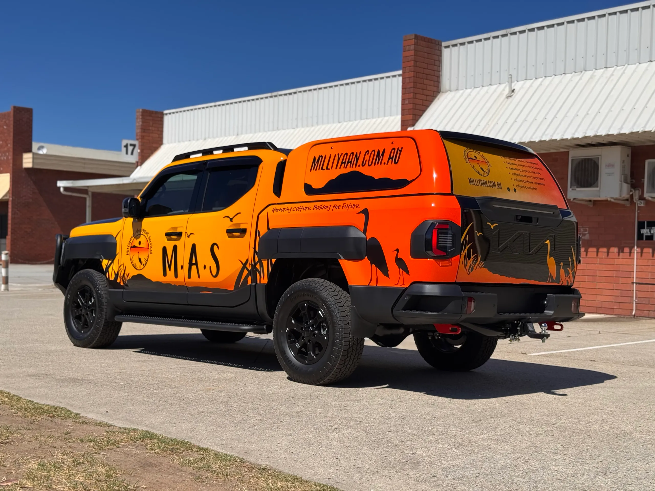 Kia Tasman with orange and black Milliyaan Aboriginal Services graphics outside the workshop