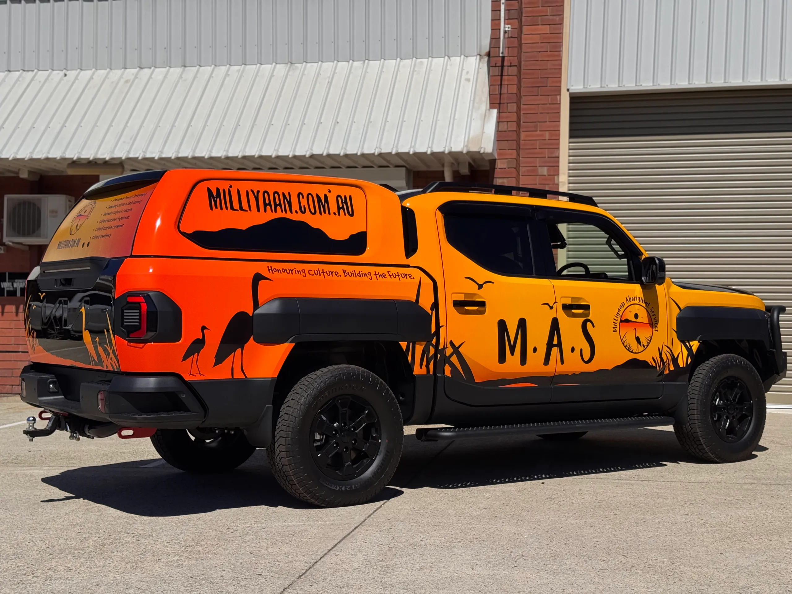 Rear-side view of the orange and yellow Milliyaan Kia Tasman and canopy outdoors