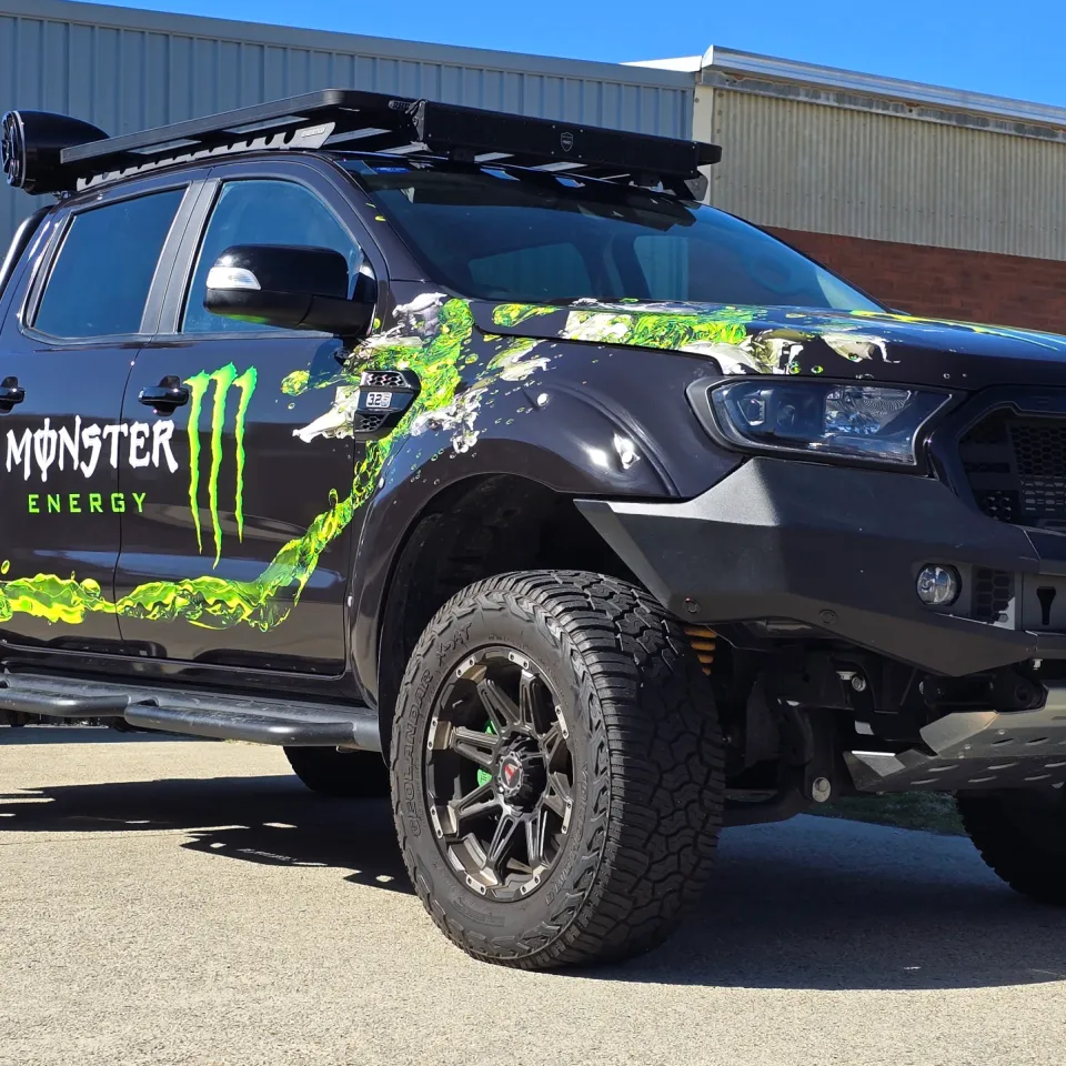 Ford Ranger with green Monster Energy graphics, off-road wheels and a roof rack outdoors