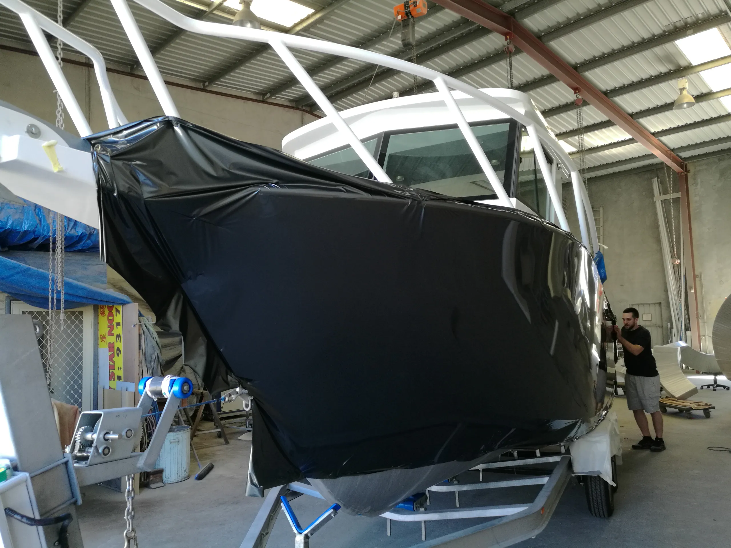 Installer beside loose charcoal film stretched across the boat hull