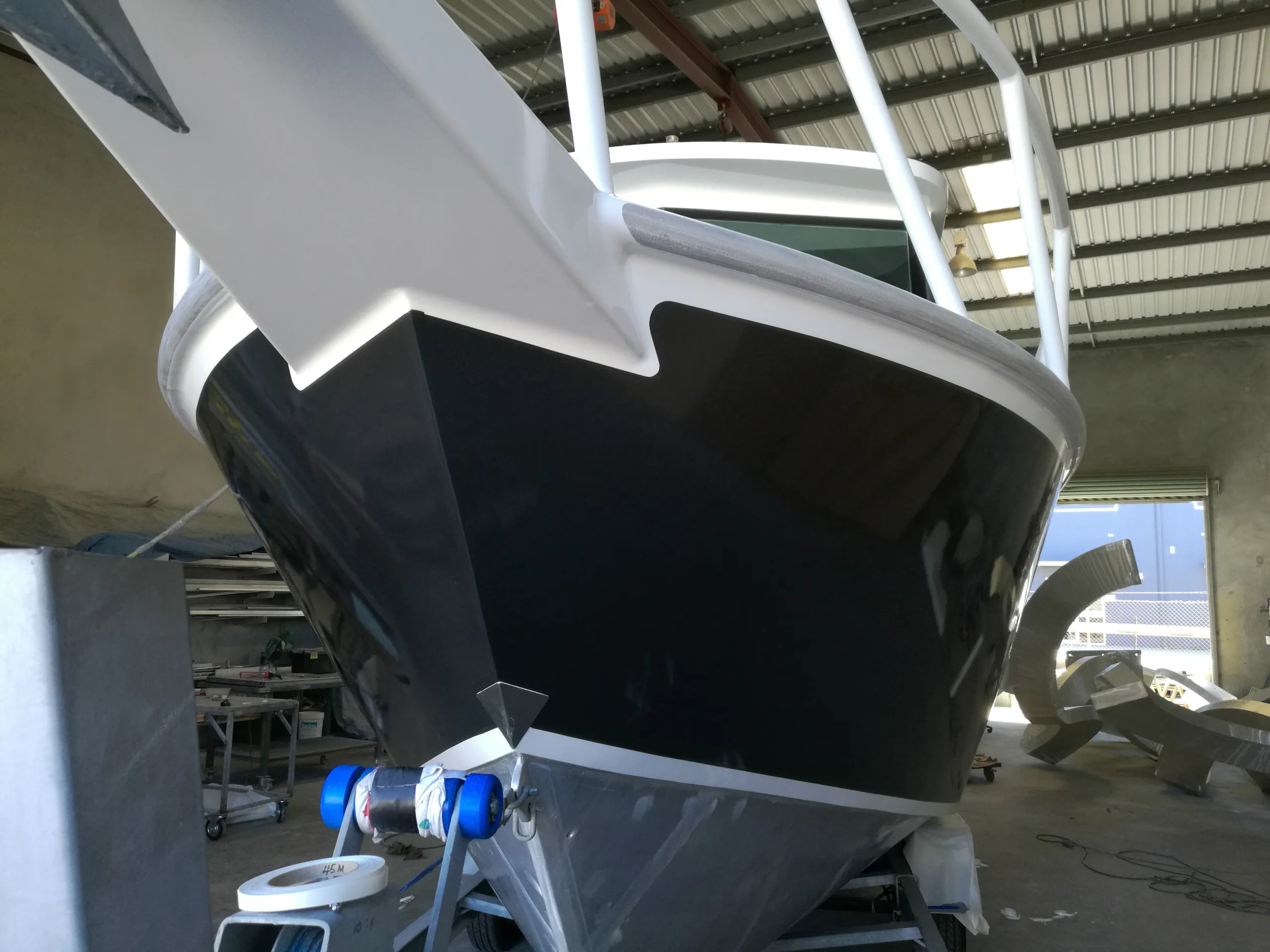 Charcoal boat bow beneath white rails and a white cabin in the workshop