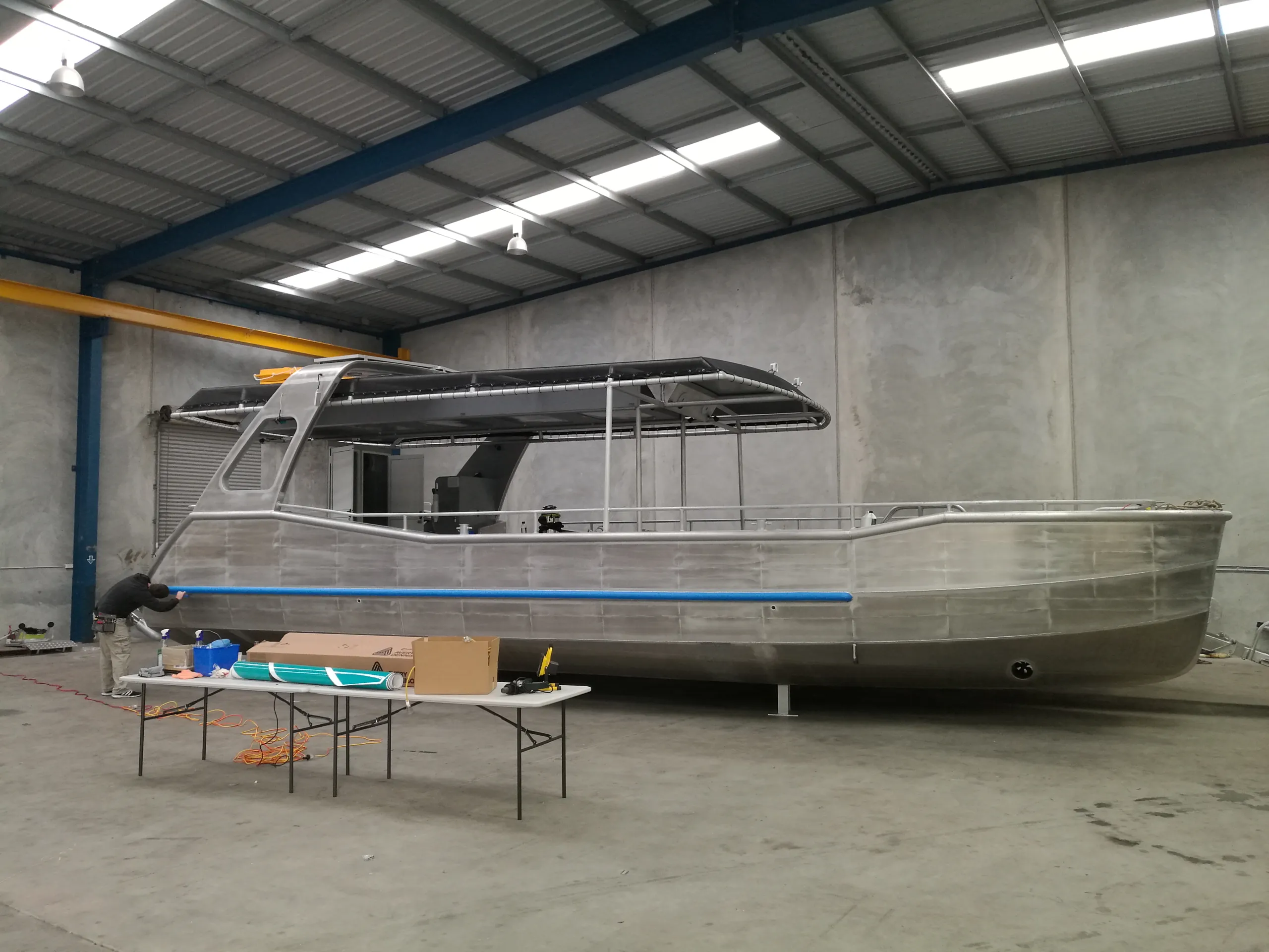 Bare aluminium passenger boat inside a shed before its wildlife wrap is fitted