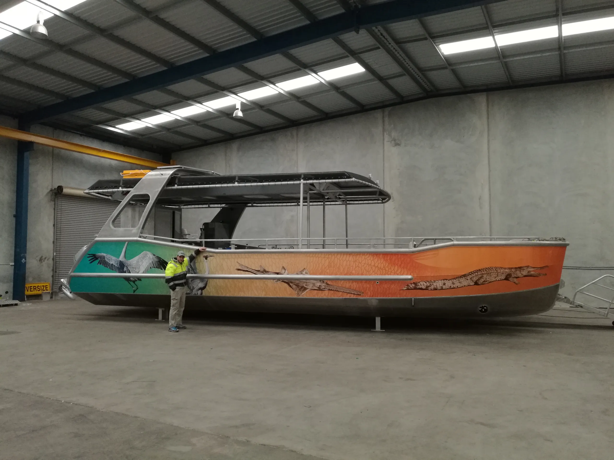 Side view of a boat with bird and crocodile graphics, with a worker standing beside the hull