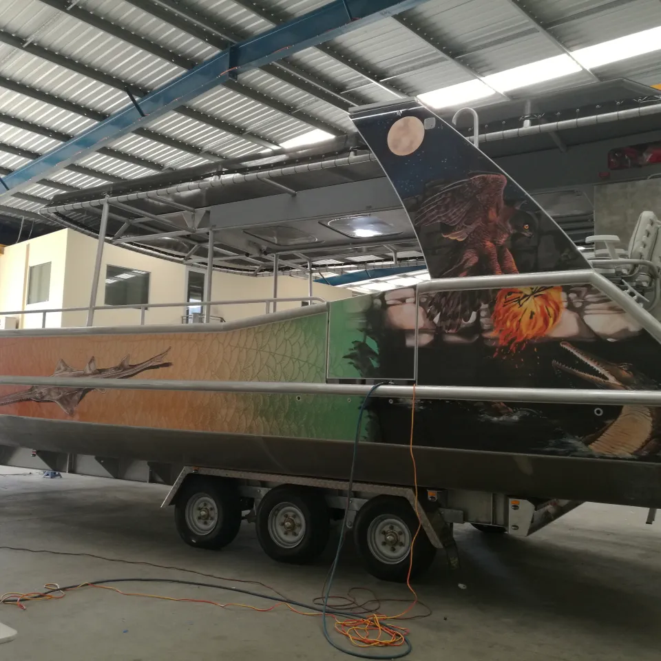 Wildlife graphics along a boat hull and cabin support, viewed from the stern quarter on its trailer