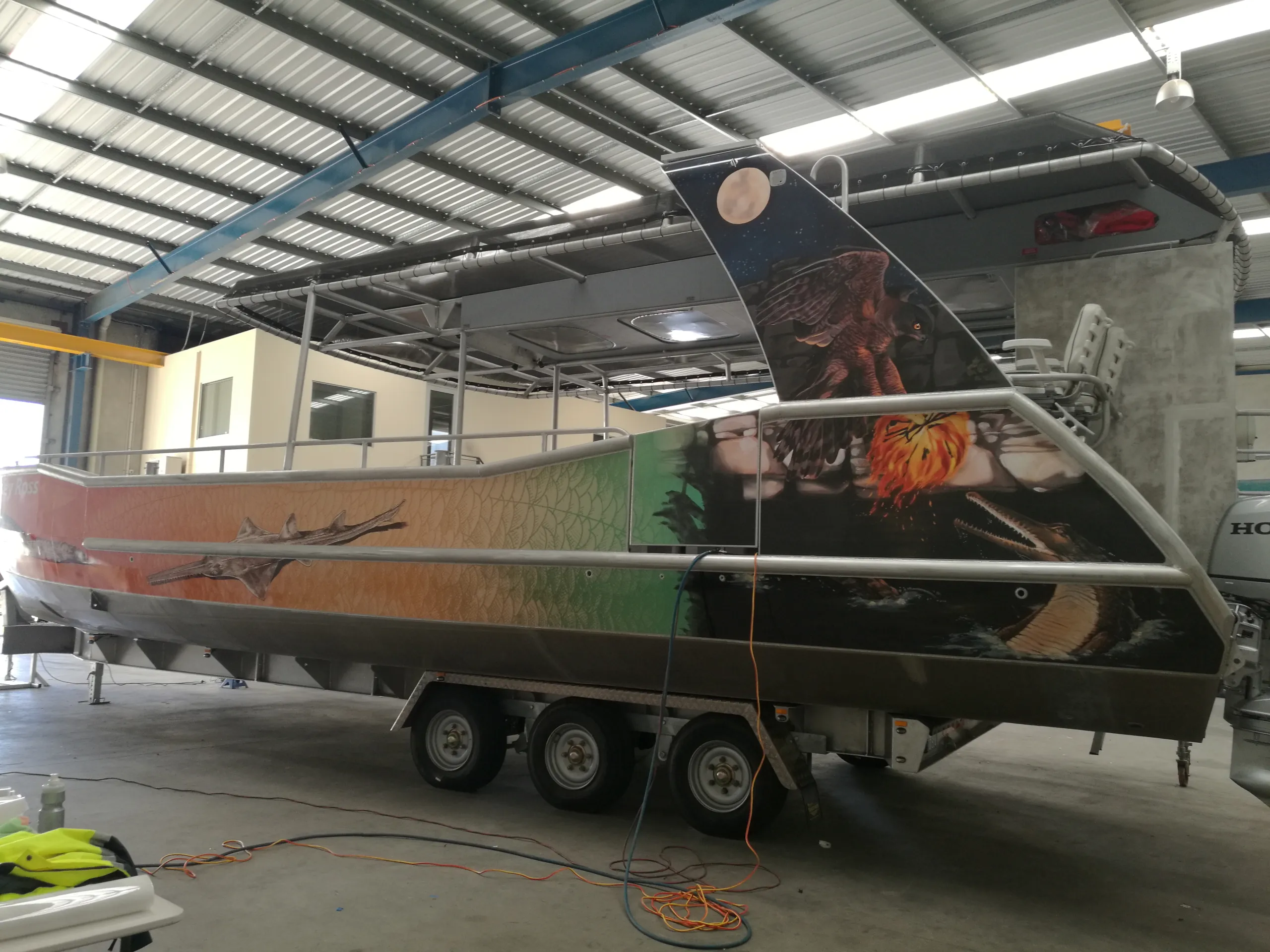 Wildlife graphics along a boat hull and cabin support, viewed from the stern quarter on its trailer