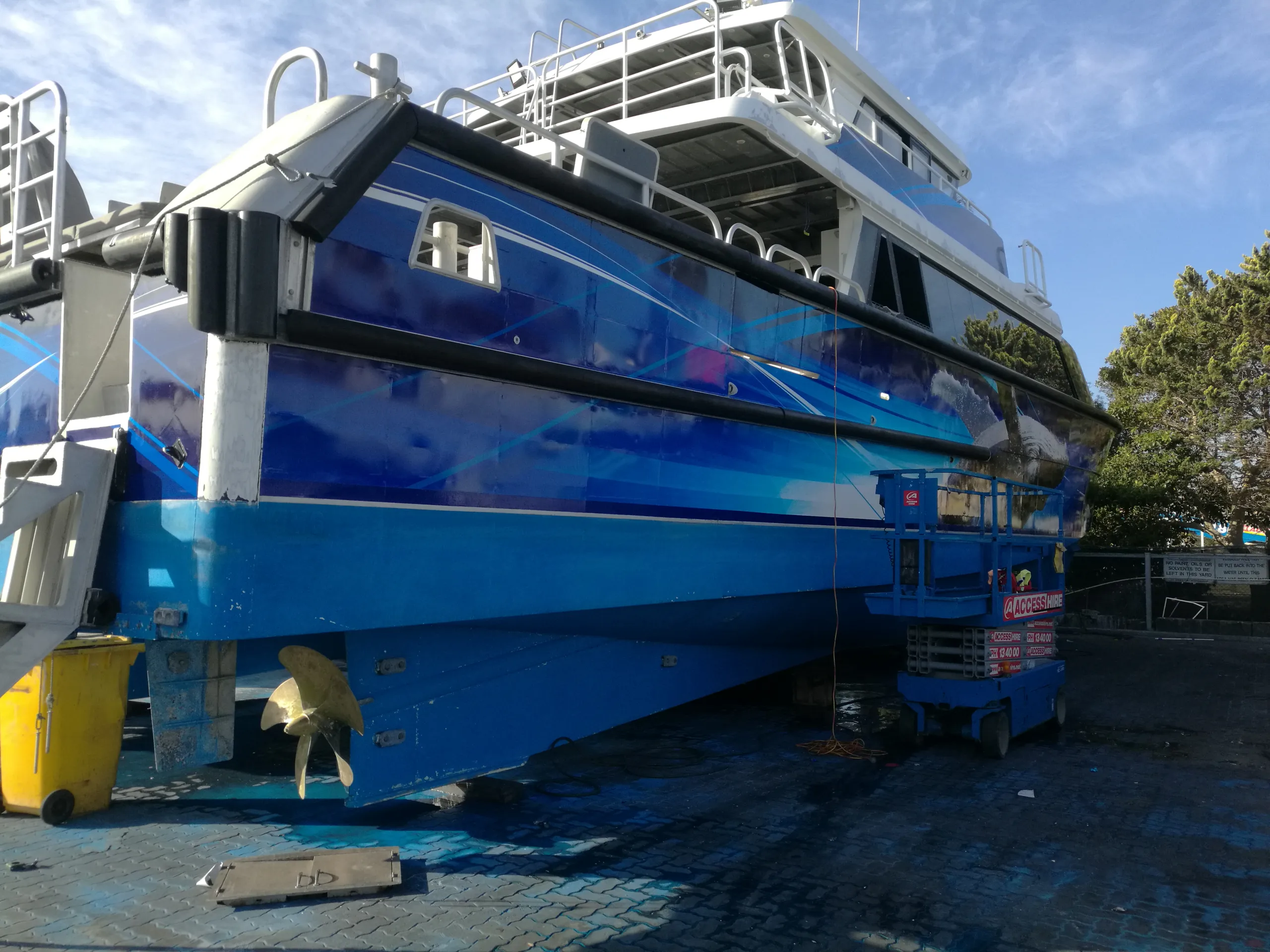 Blue graphics on the Naturaliste Charters catamaran stern quarter beside a scissor lift