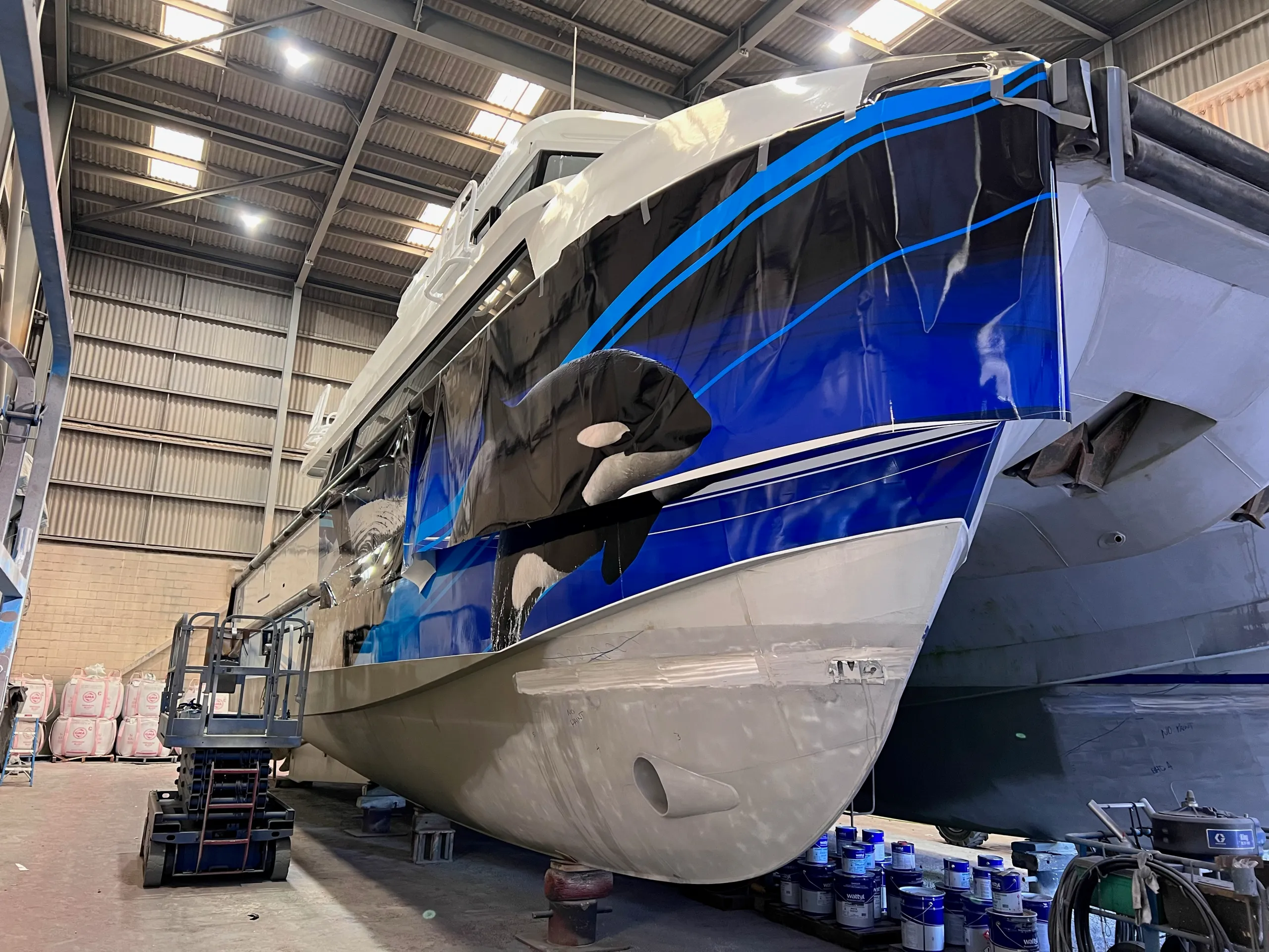 Orca hull artwork partly fitted around the Naturaliste Charters catamaran bow in a shed