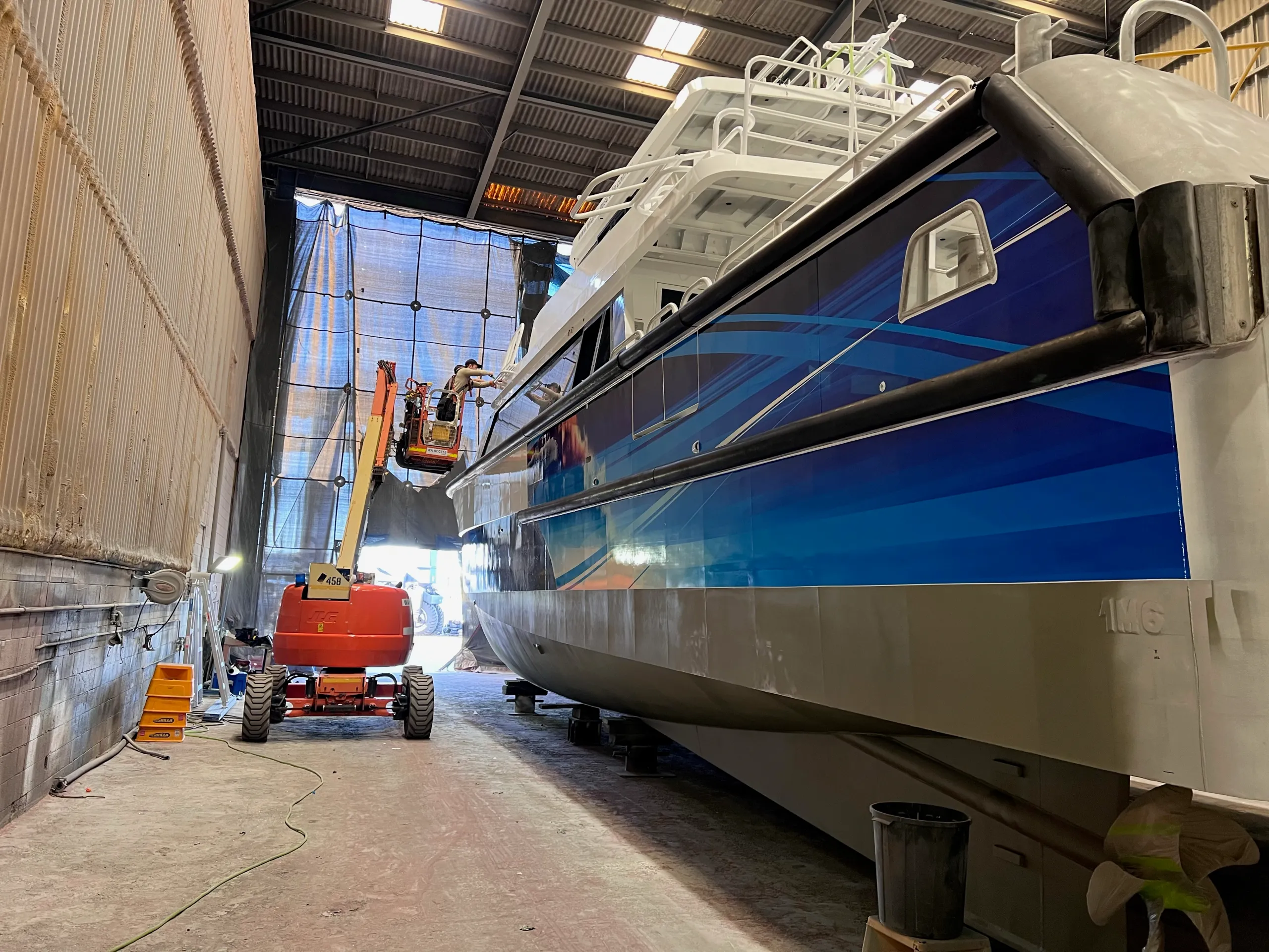 View along the Naturaliste Charters catamaran hull towards an installer on a boom lift