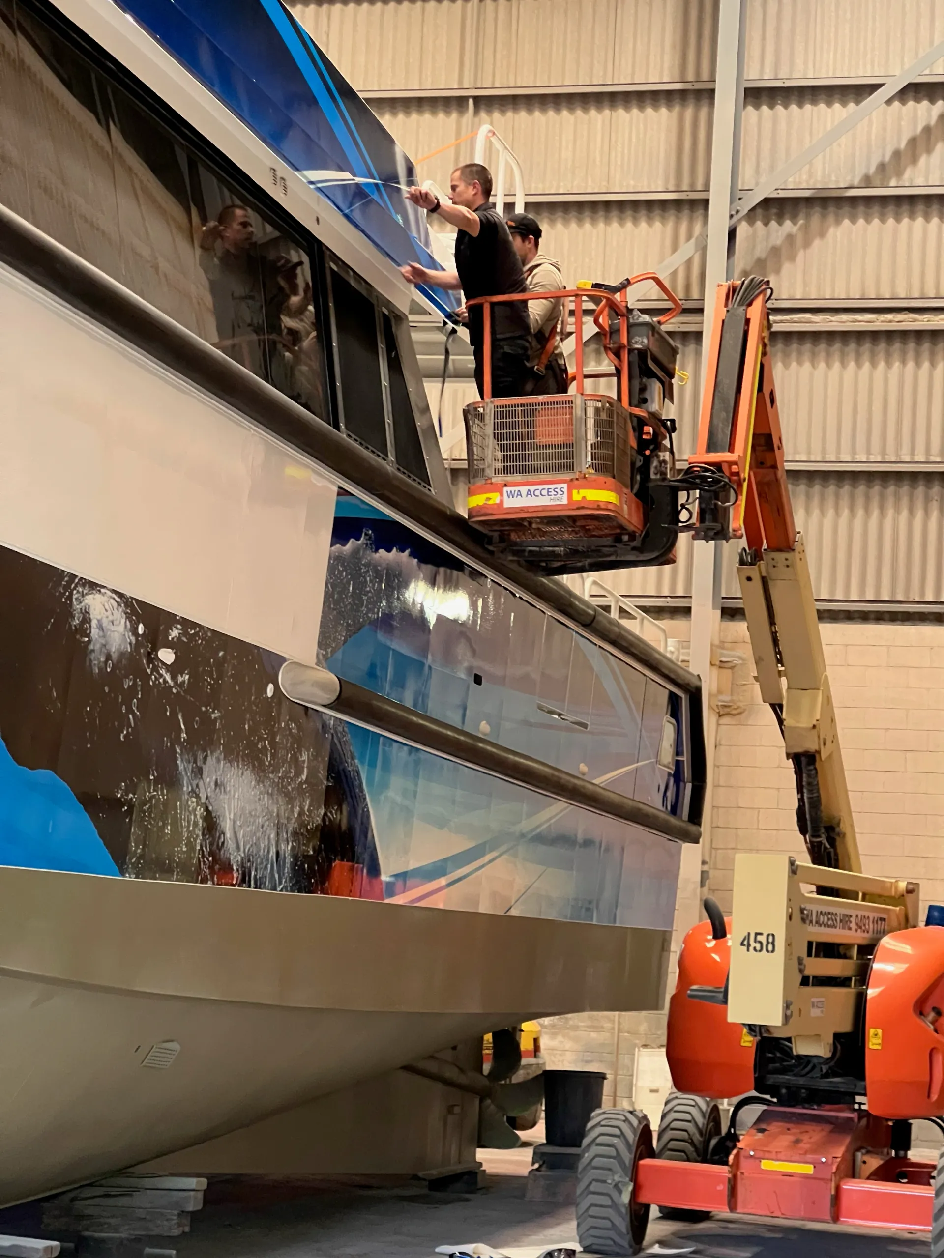 Installers fitting graphics above the Naturaliste Charters catamaran windows from a boom lift