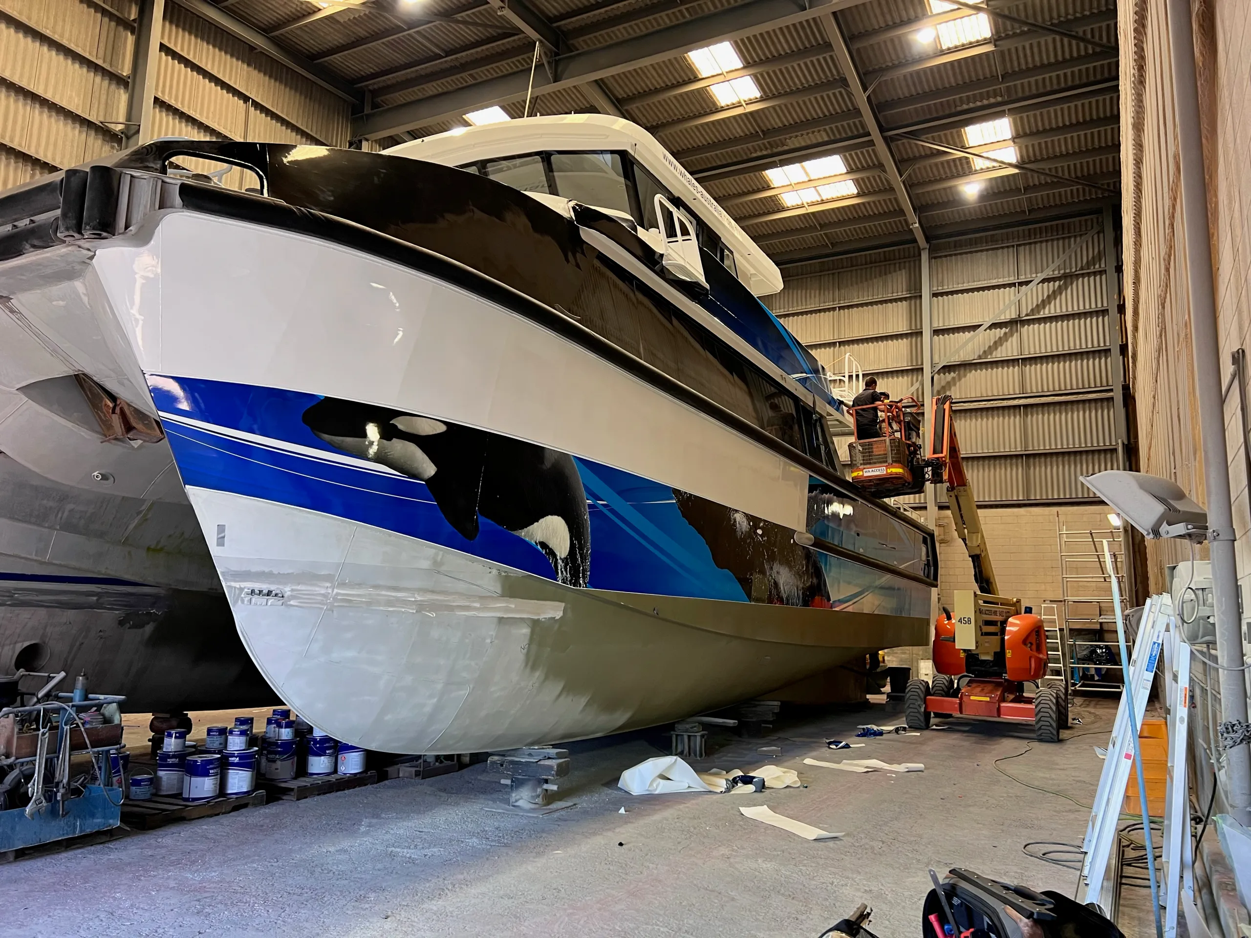 Naturaliste Charters catamaran bow during wrapping, with installers working from a boom lift