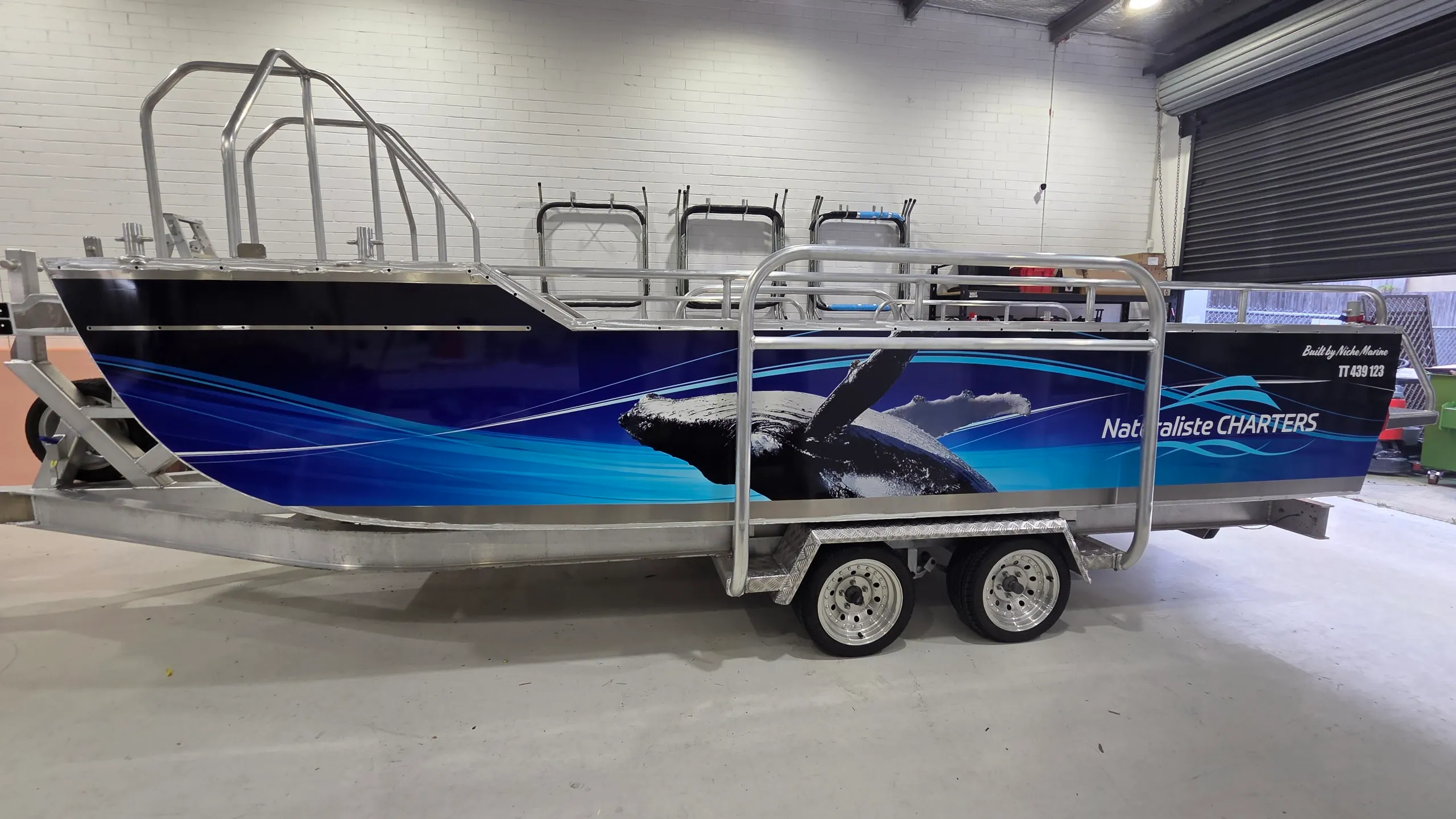 Naturaliste Charters tender with blue whale graphics on a tandem-axle trailer in the workshop