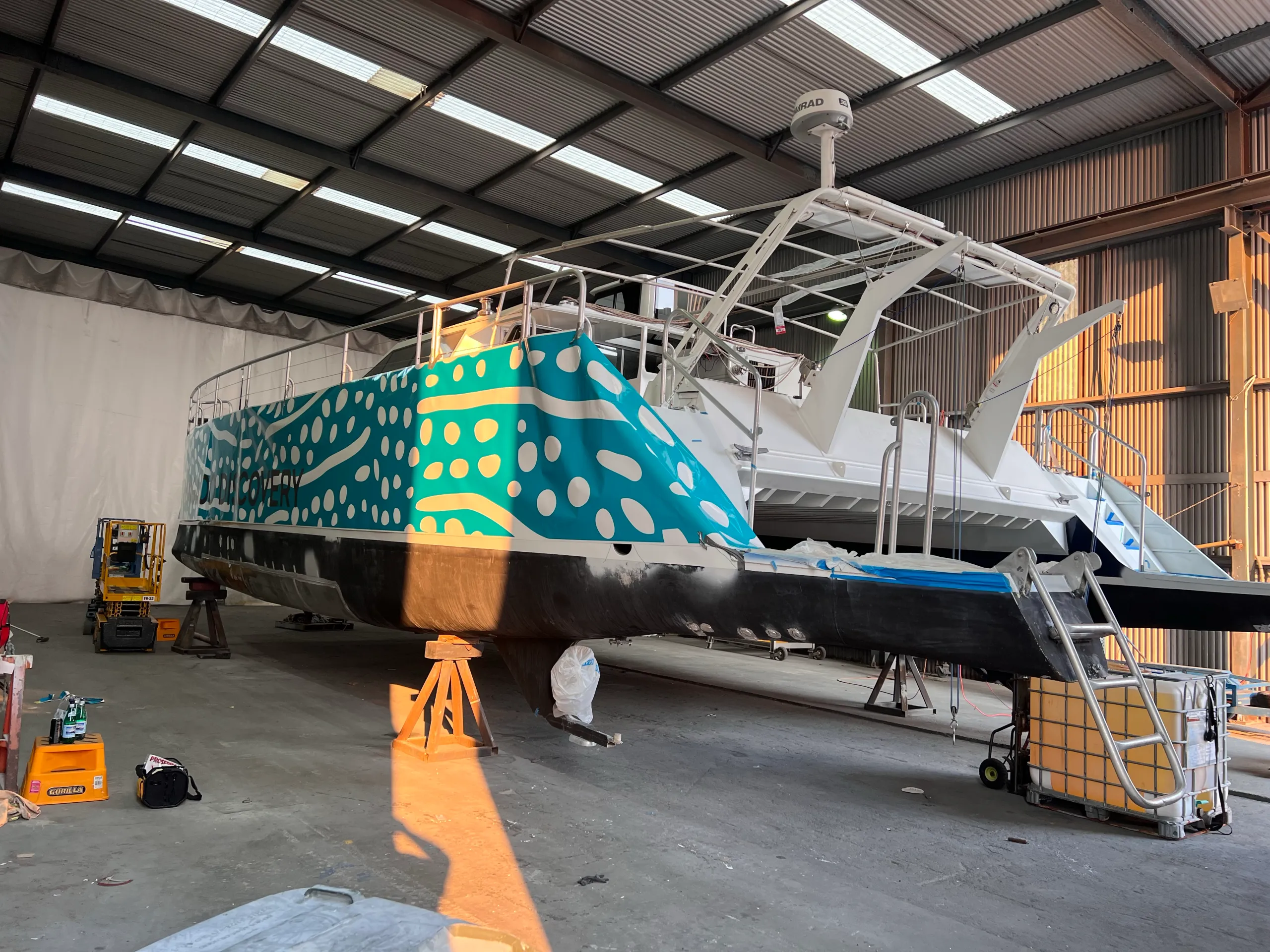 Catamaran stern quarter with turquoise and white spotted graphics and loose film during installation