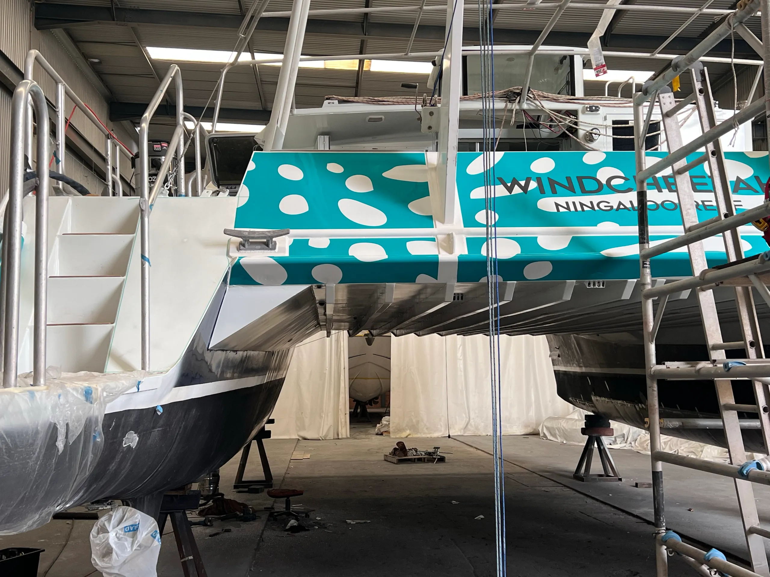 Turquoise and white graphics across the catamaran stern bridge between the two hulls during installation