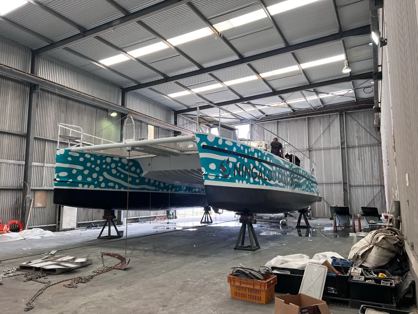 Ningaloo Discovery catamaran in a shed with turquoise spotted graphics and people on the upper deck