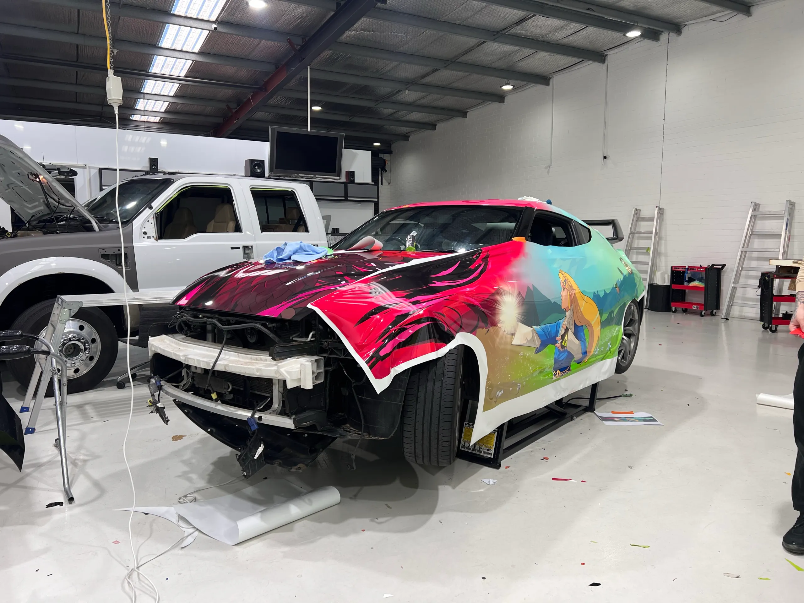 Nissan 370Z with its front bumper removed and printed film partly fitted in the workshop