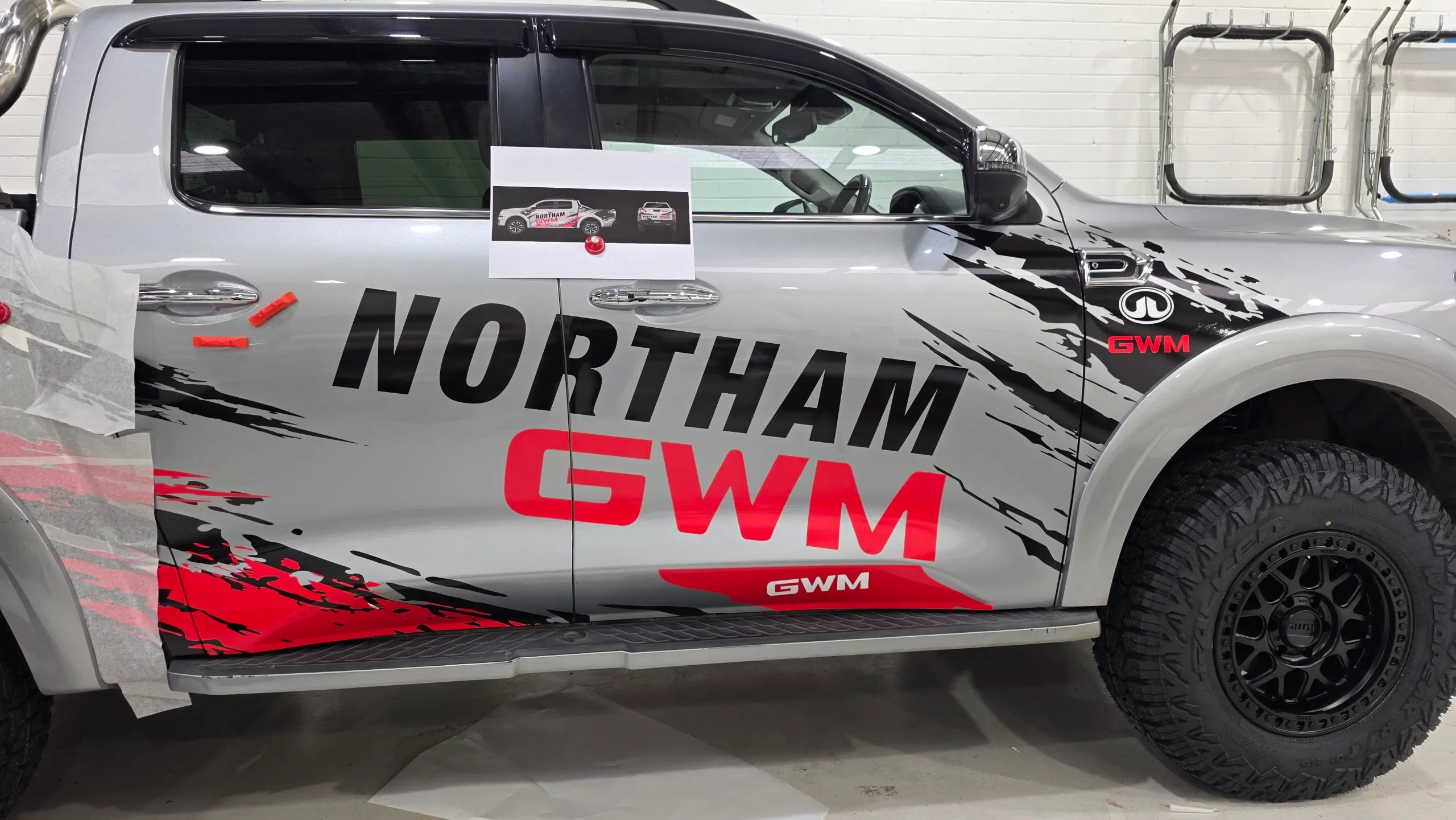 Northam GWM graphics being fitted to a silver Cannon ute with an artwork proof taped to the door