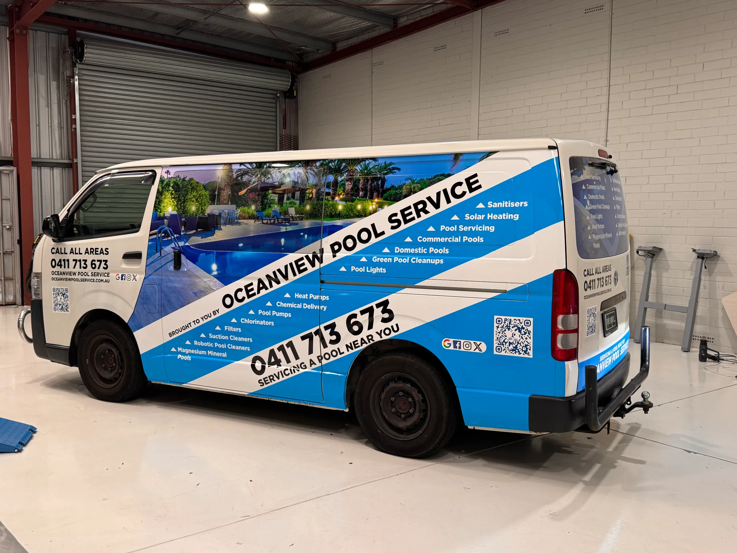 Oceanview Pool Service Toyota HiAce with blue and white graphics and a printed pool image in the workshop