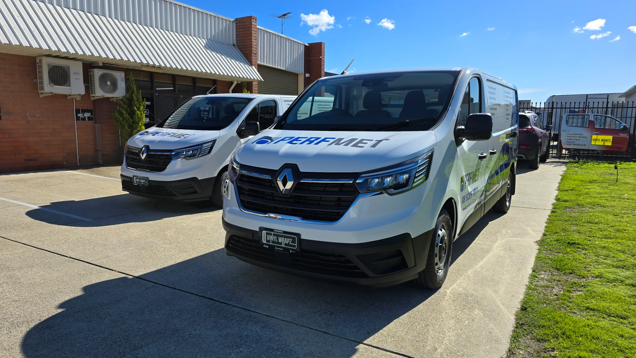 Two white Renault Trafic vans with blue Perfmet graphics outside the workshop