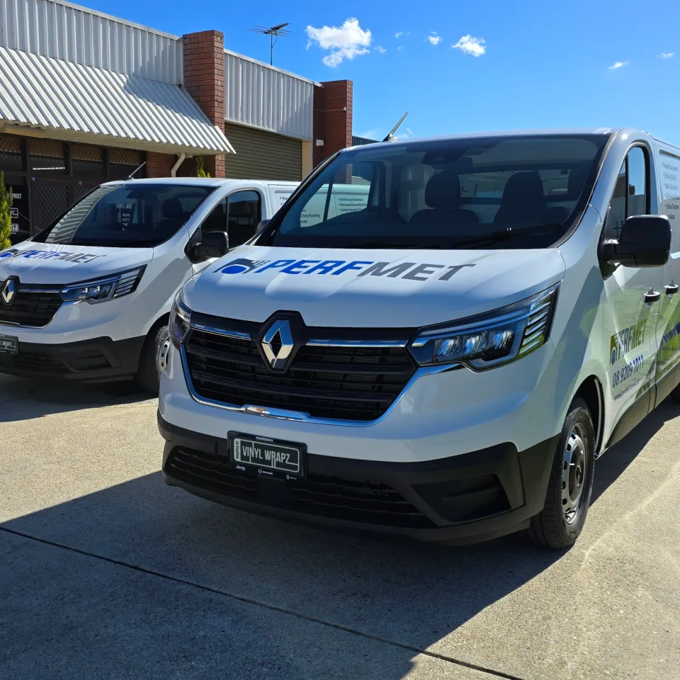 Two white Renault Trafic vans with blue Perfmet graphics outside the workshop